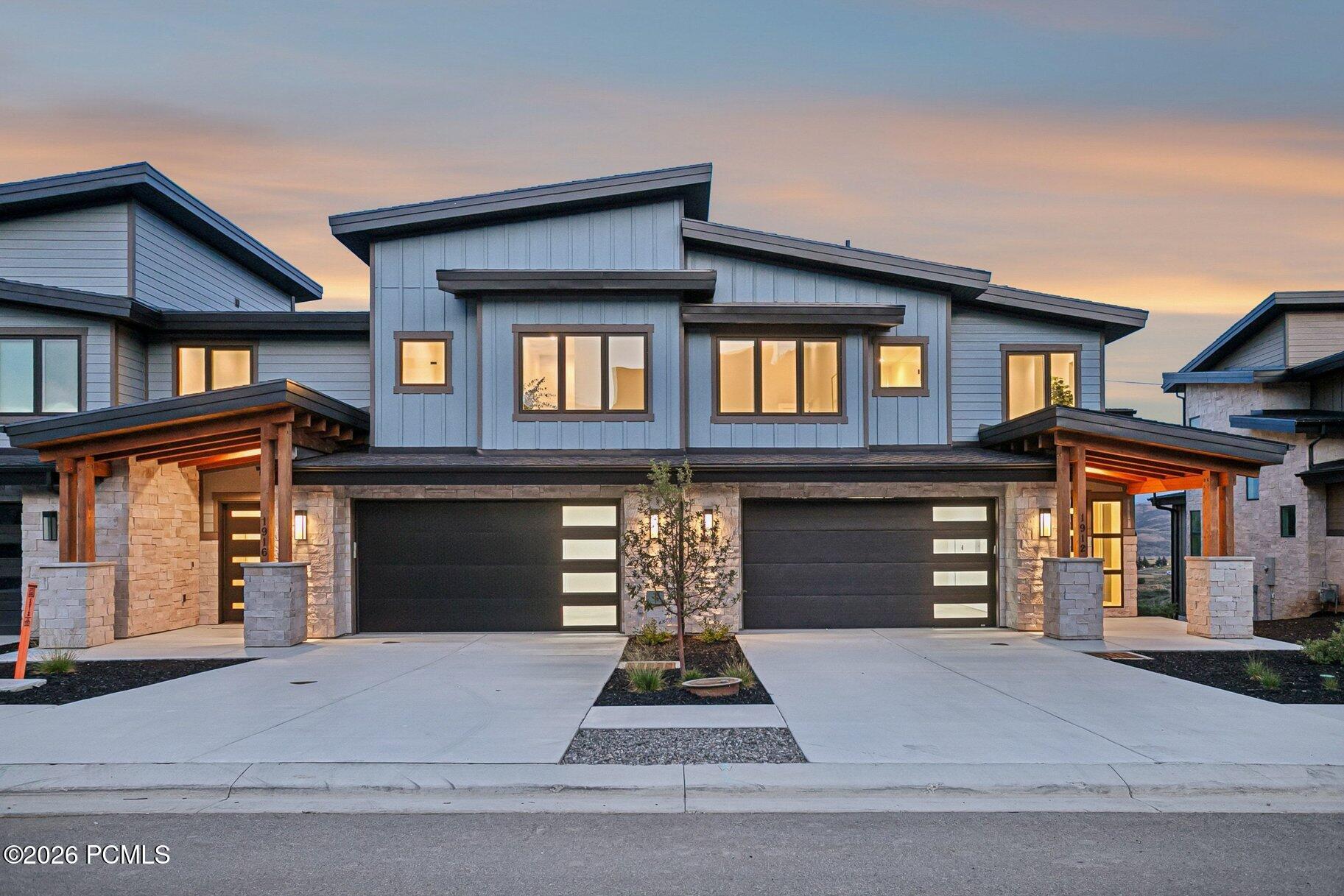 Modern two-story home with stone accents, twin garage doors, and warmly lit windows at dusk.