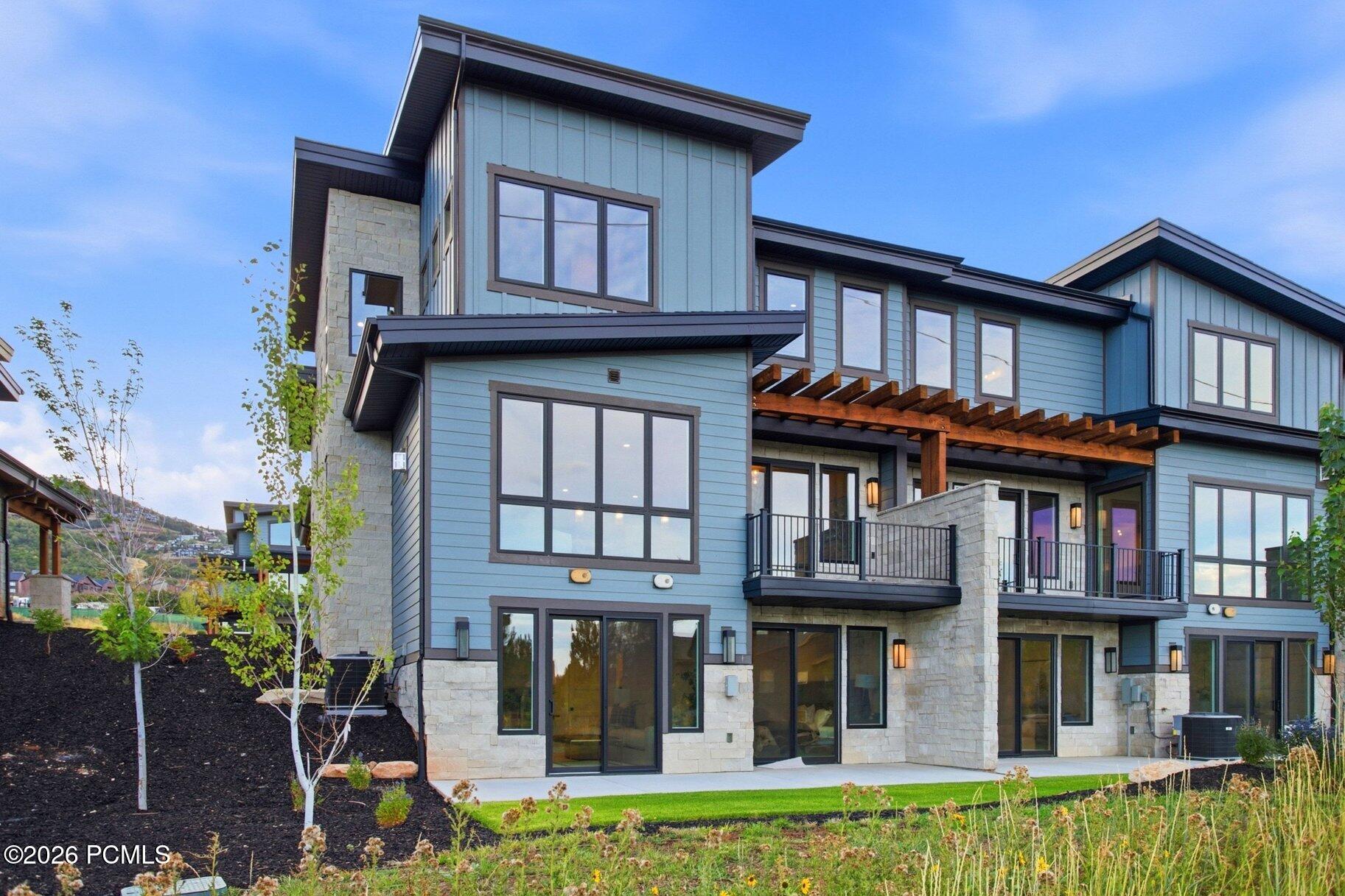 Contemporary blue-sided home with stone accents, balconies, and a timber pergola over the patio.