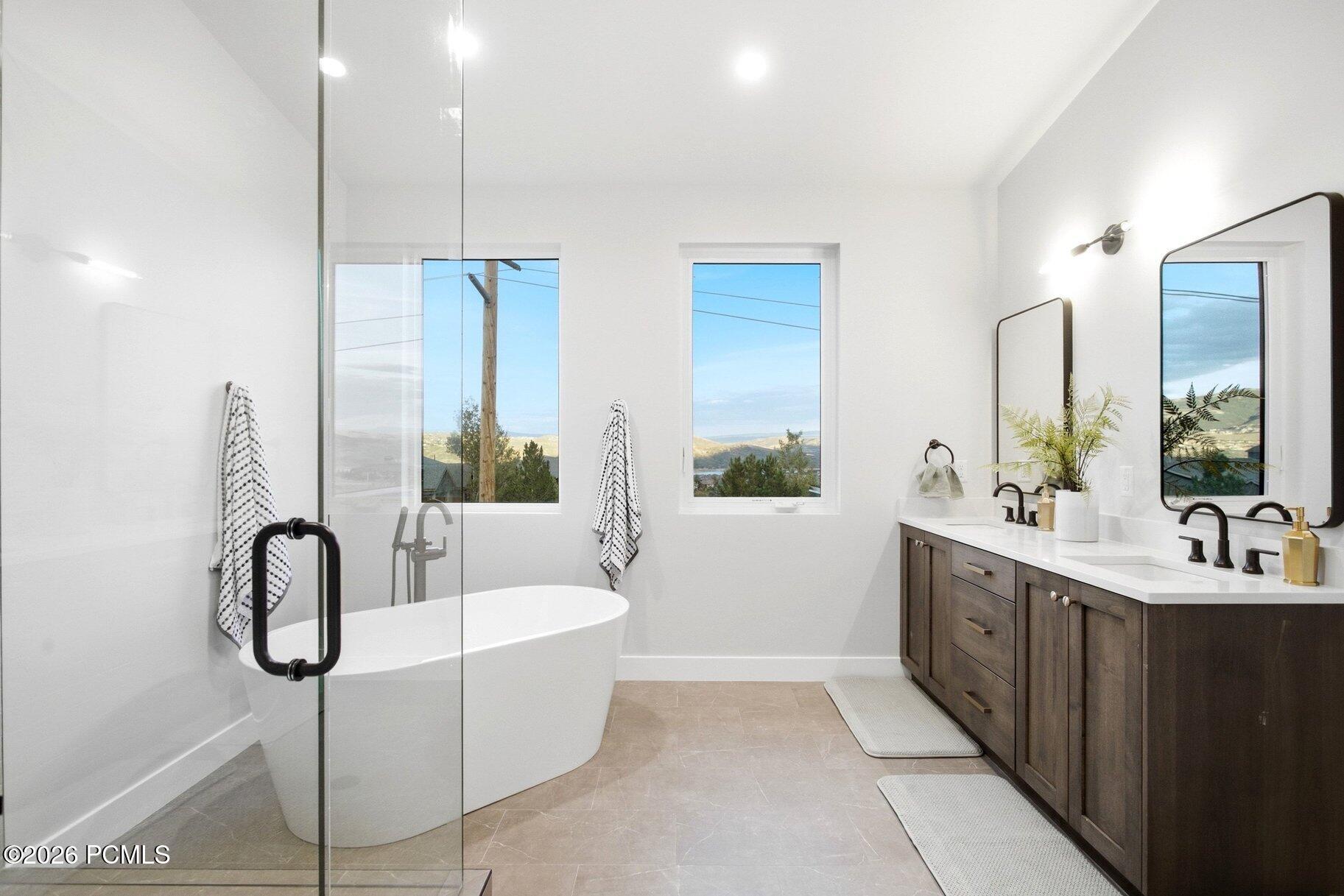 Modern bathroom with a freestanding tub, dark double vanity, and windows overlooking distant hills.