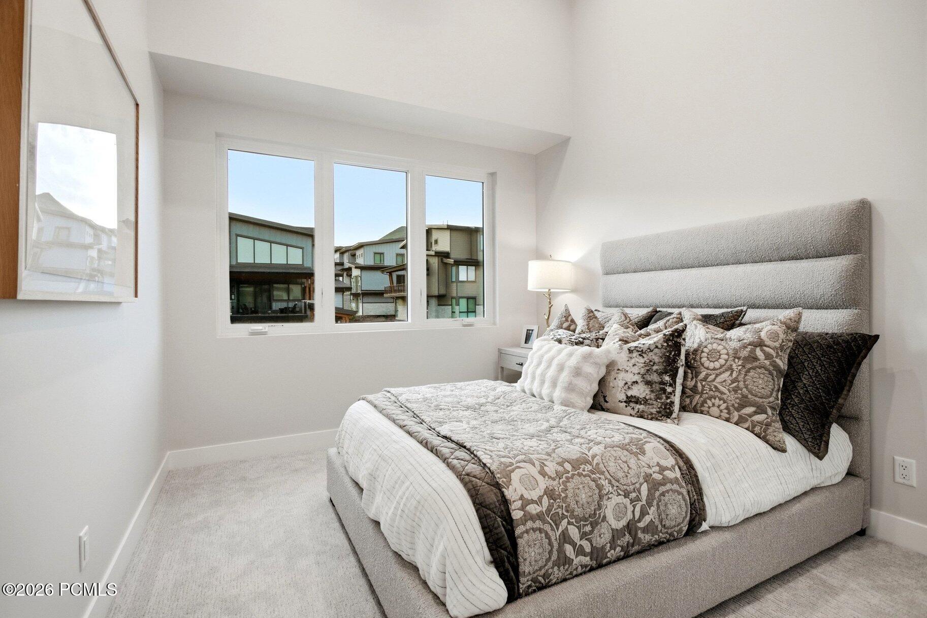 Staged bedroom with a large upholstered bed and patterned bedding beside a wide window.