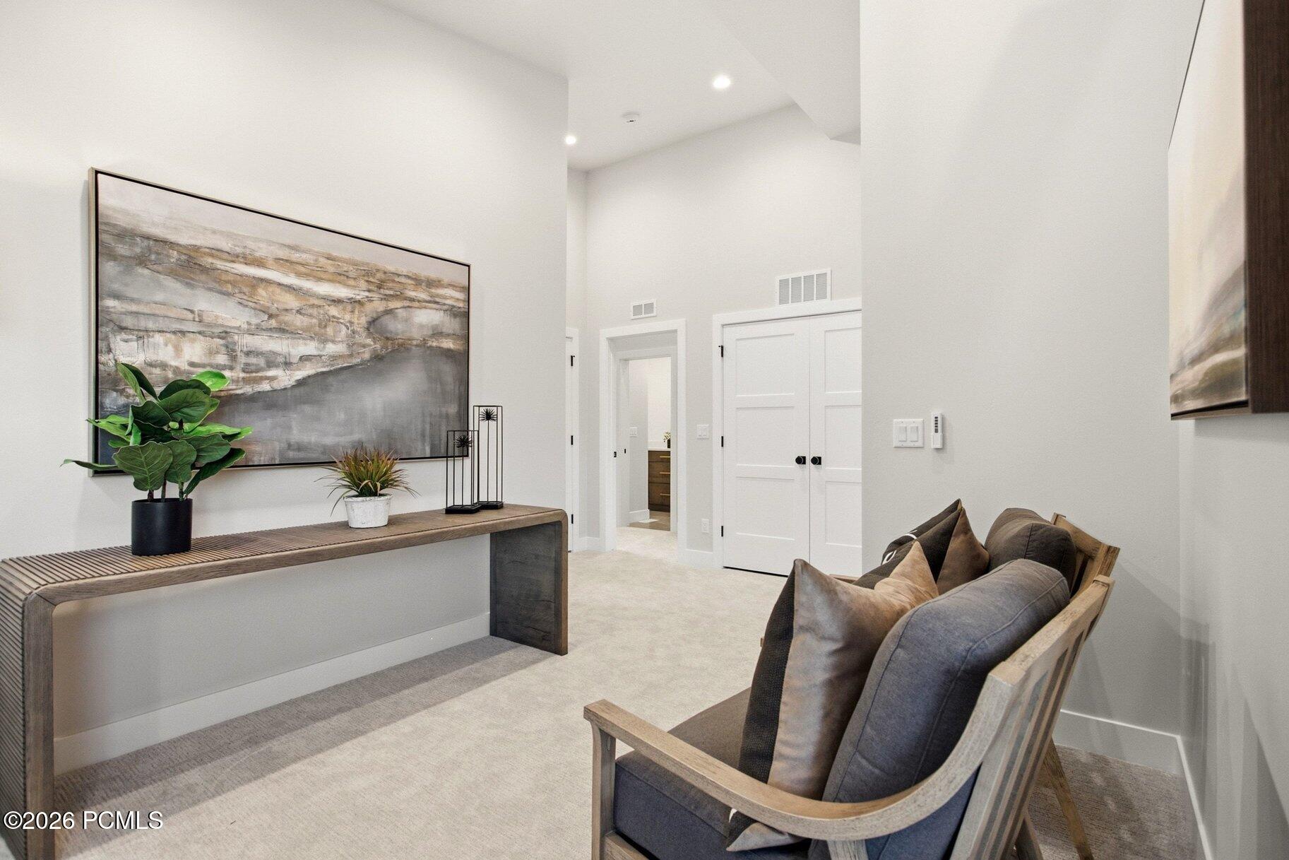 Furnished sitting area with gray cushioned bench, wood console table, potted plants, and abstract wall art.