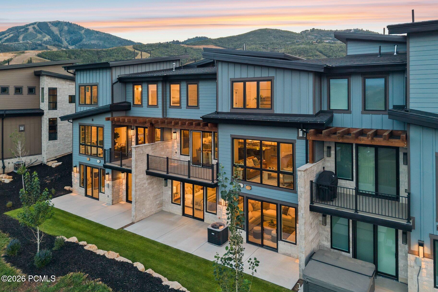 Modern blue multi-level home with stone accents and balconies, backed by mountain ridges at dusk.