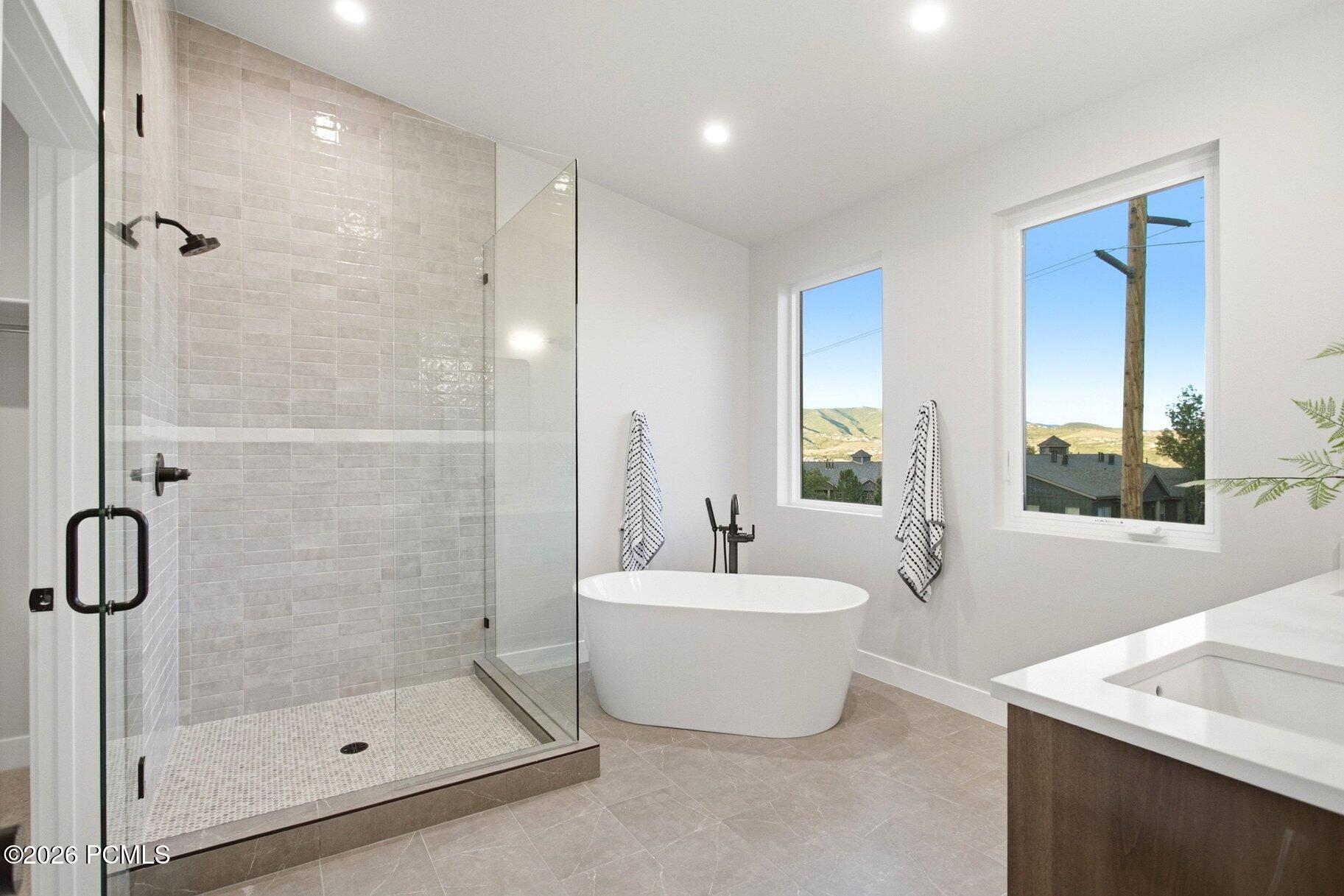 Modern bathroom with a glass-enclosed tiled shower, freestanding tub, and windows overlooking hills.
