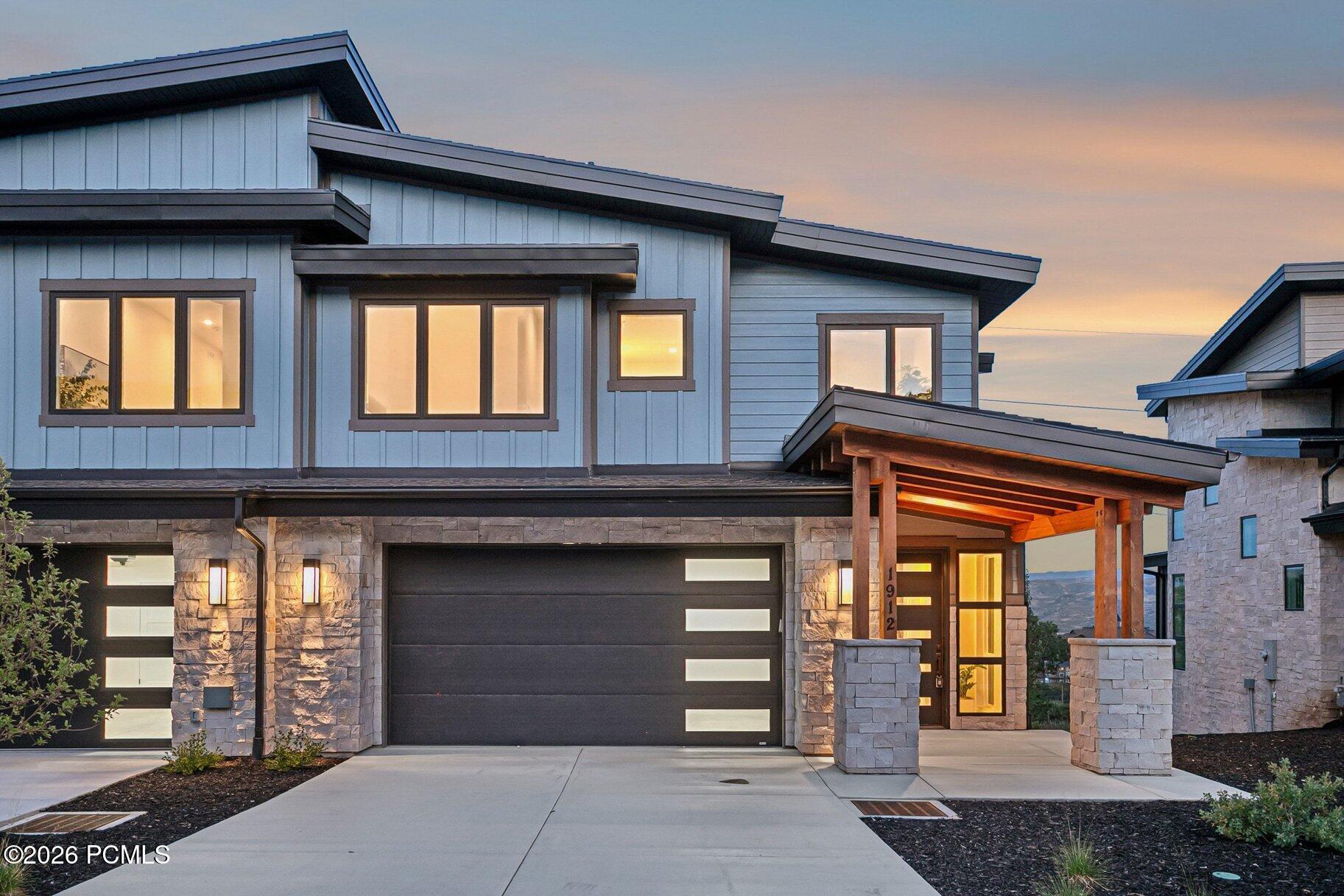Modern two-story home with a stone facade, wide garage, and warmly lit covered entry at dusk.