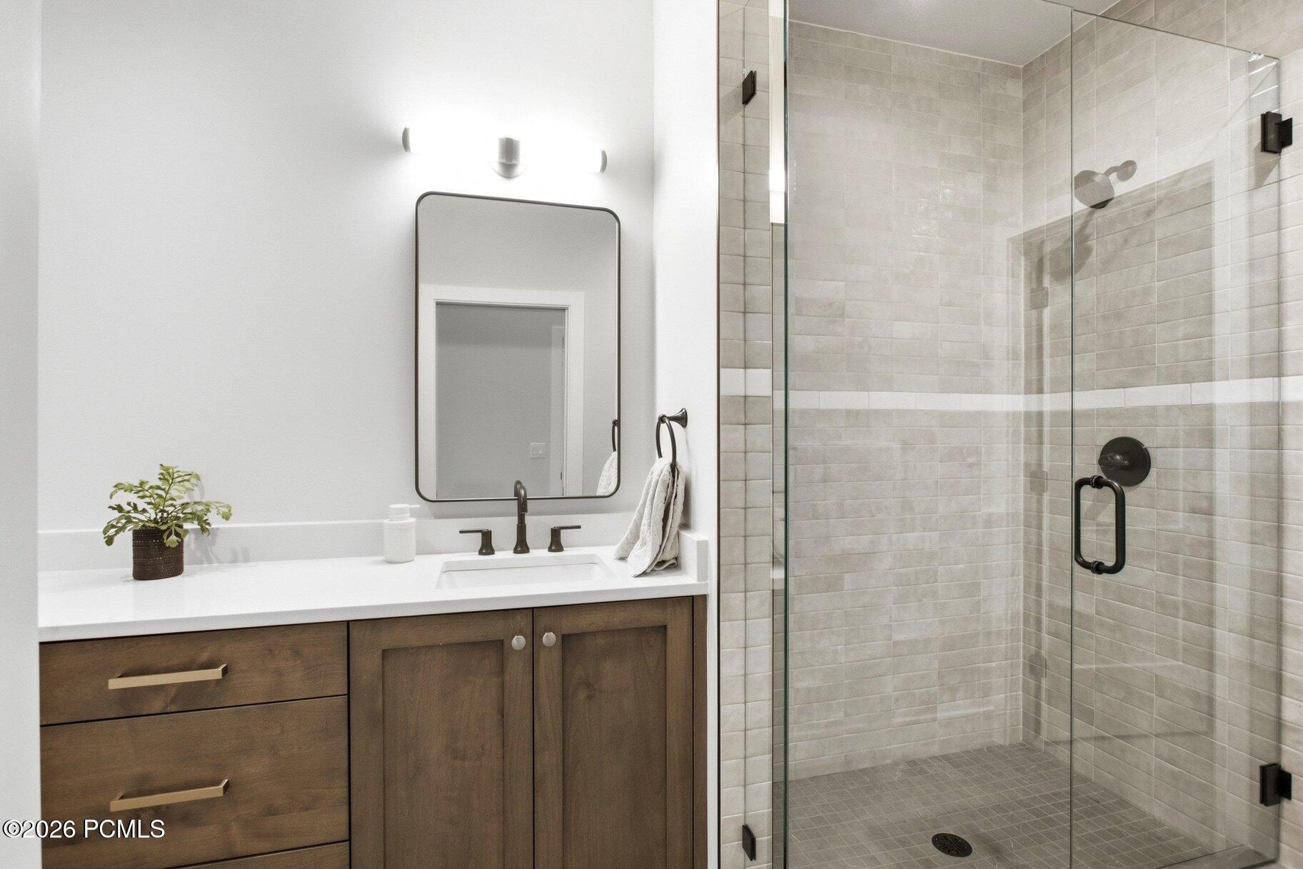 Bathroom vanity with dark wood cabinets beside a glass-enclosed, light-tile shower.