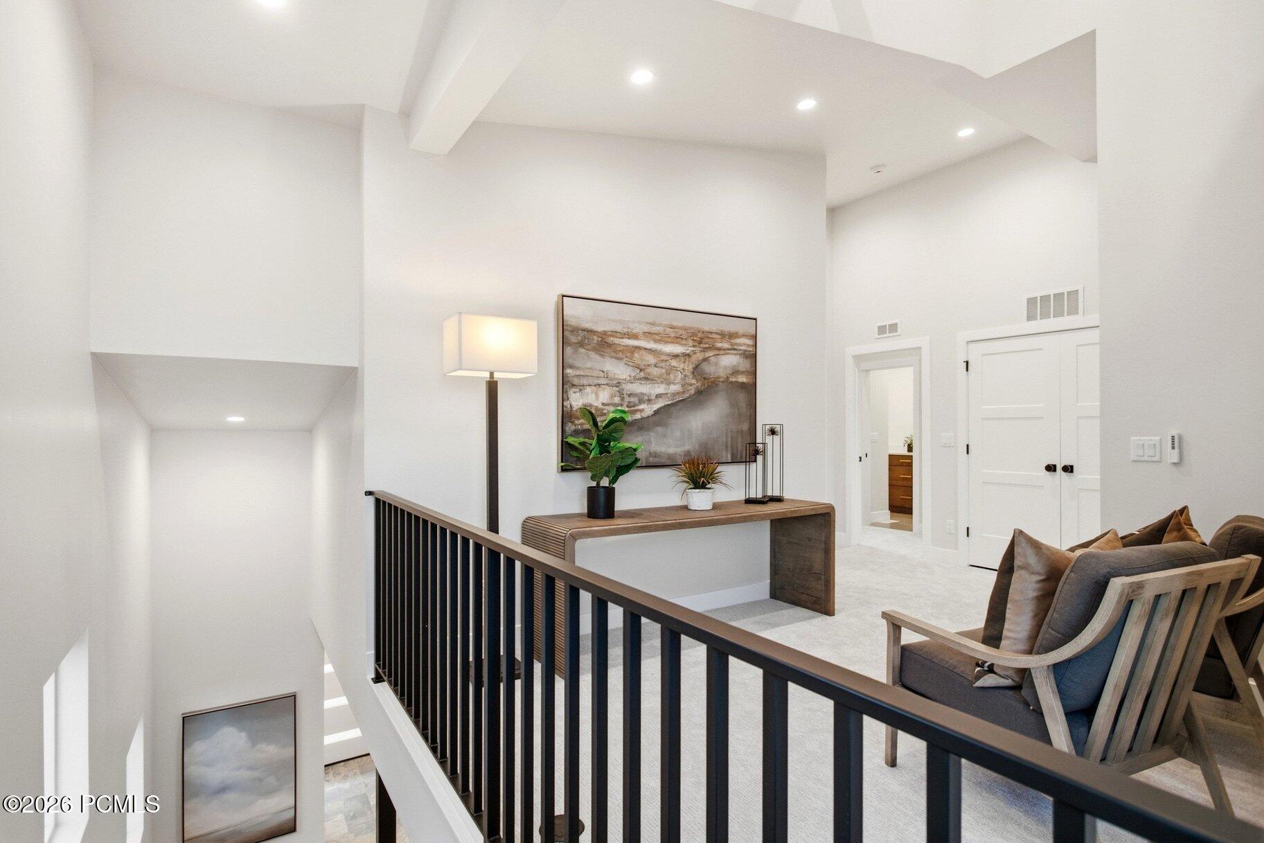 Upper-level landing with black railing, wood console table, and lounge chairs overlooking a staircase.