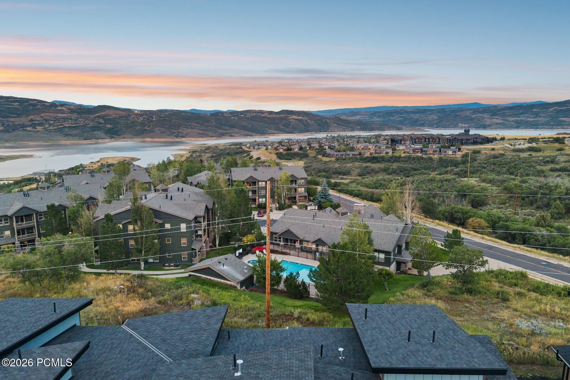 Aerial view of homes and a community pool overlooking a reservoir and mountain range at sunset.