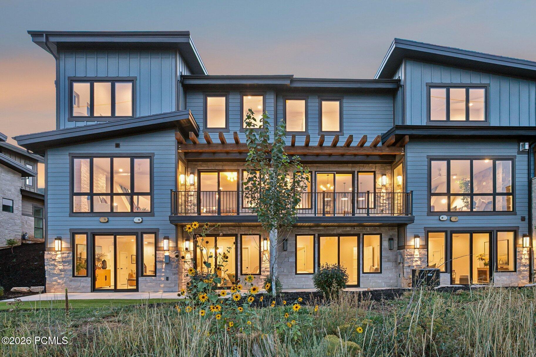 Modern blue-sided home at dusk with a stone facade, balcony, and garden.