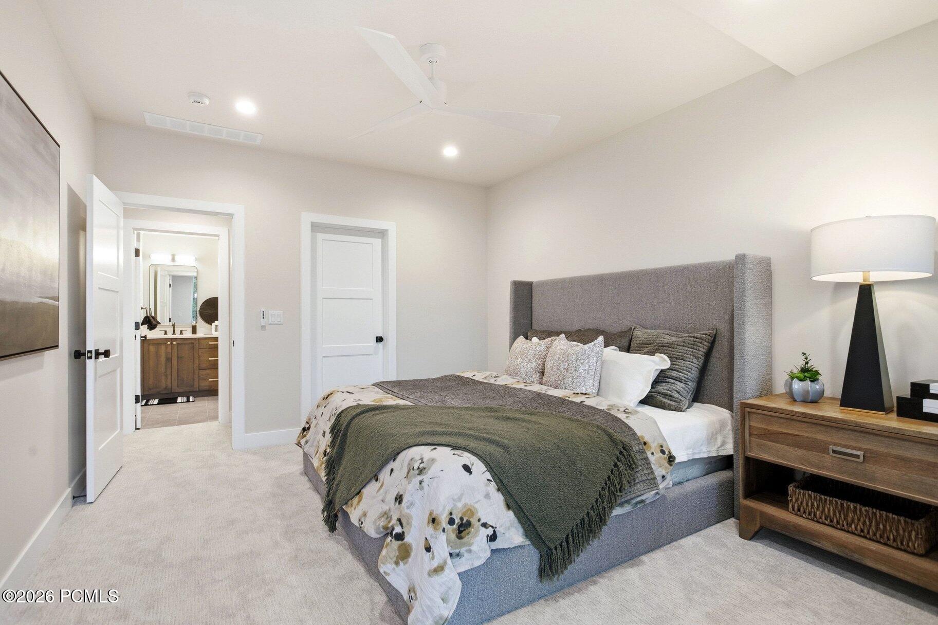 Staged bedroom with a gray upholstered bed, layered bedding, and an open doorway to a bathroom.
