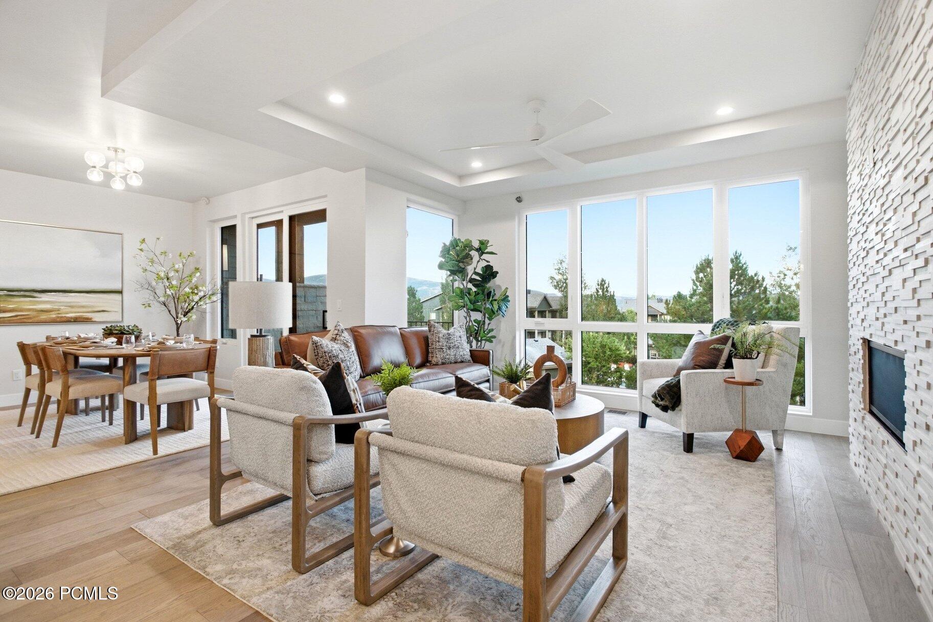 Open-plan living and dining room with large windows, a textured fireplace wall, and neutral furnishings.