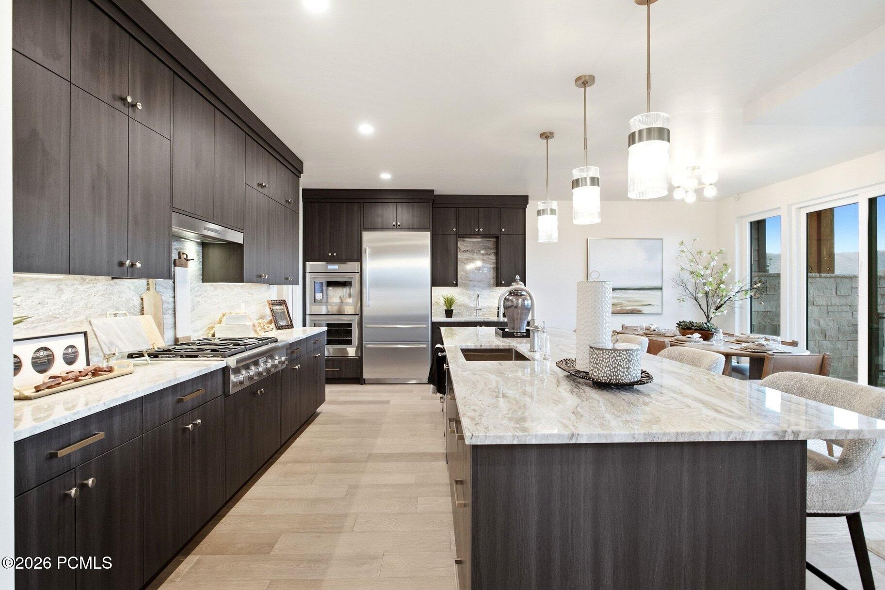 Kitchen with dark cabinetry, stainless appliances, and a large veined stone island beside the dining area.