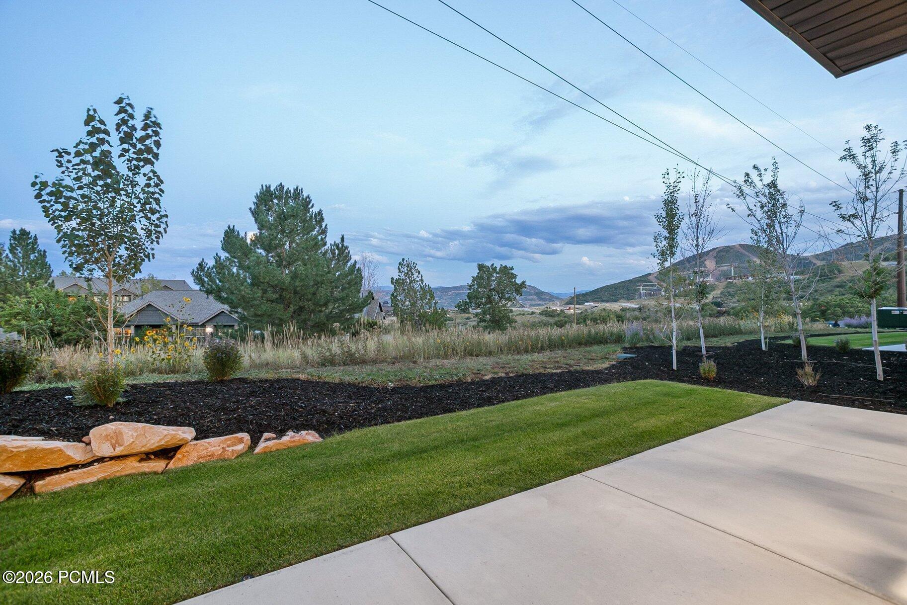 Landscaped yard and patio with young trees, nearby homes, and distant hills.