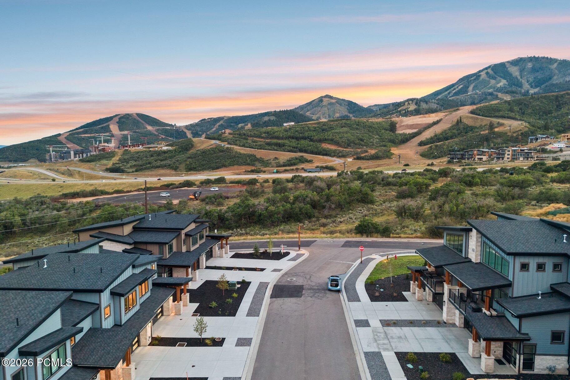 Modern homes along a neighborhood street with mountain ski slopes beneath a colorful sunset.