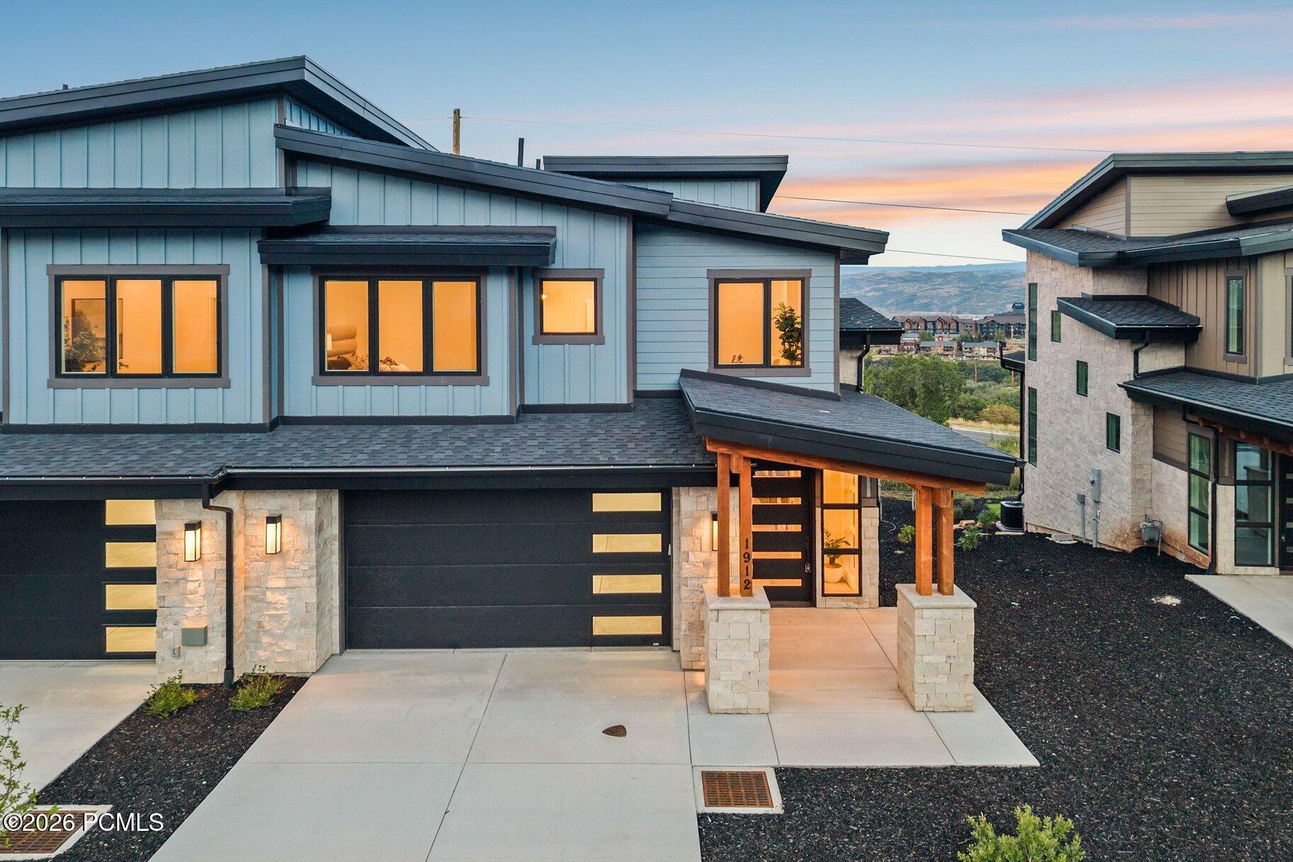 Modern blue-gray home with stone accents and a covered entrance glowing at dusk.