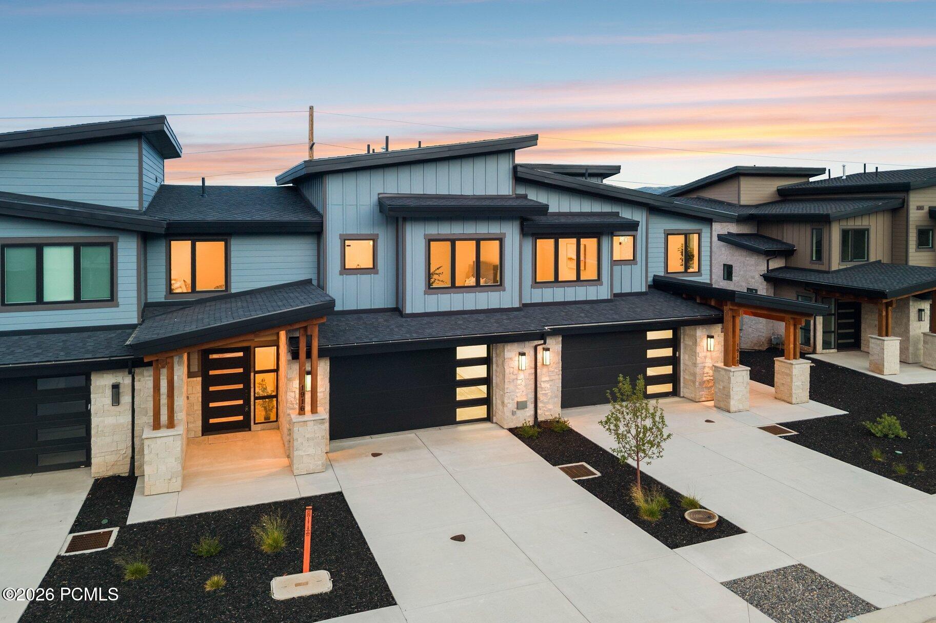 Modern blue-gray home with stone accents and illuminated windows at dusk.