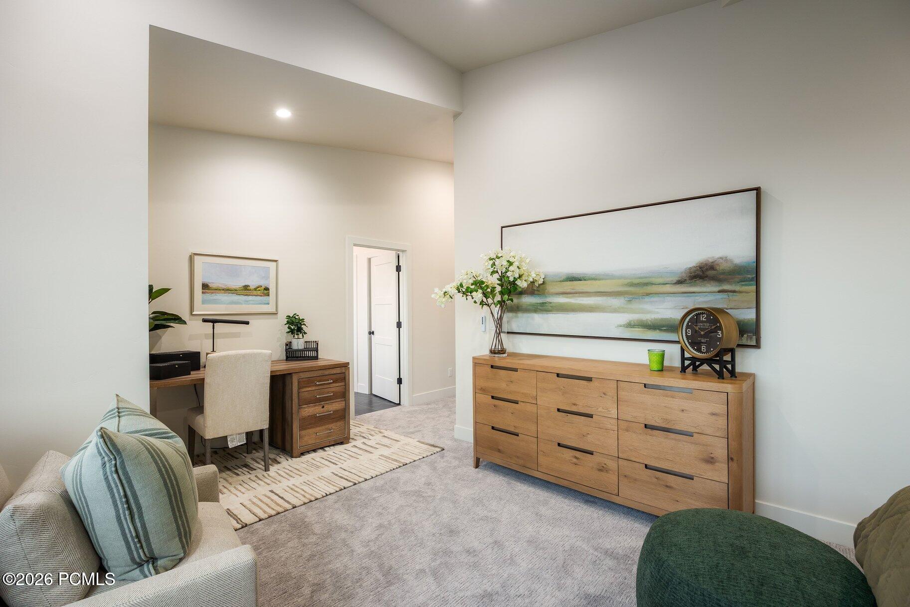 Living room with a desk nook, light sofa, and wide wooden dresser beneath landscape artwork.