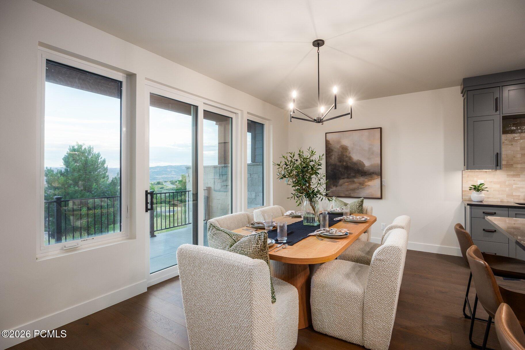 Dining room with a wood table, upholstered chairs, and large windows overlooking distant hills.
