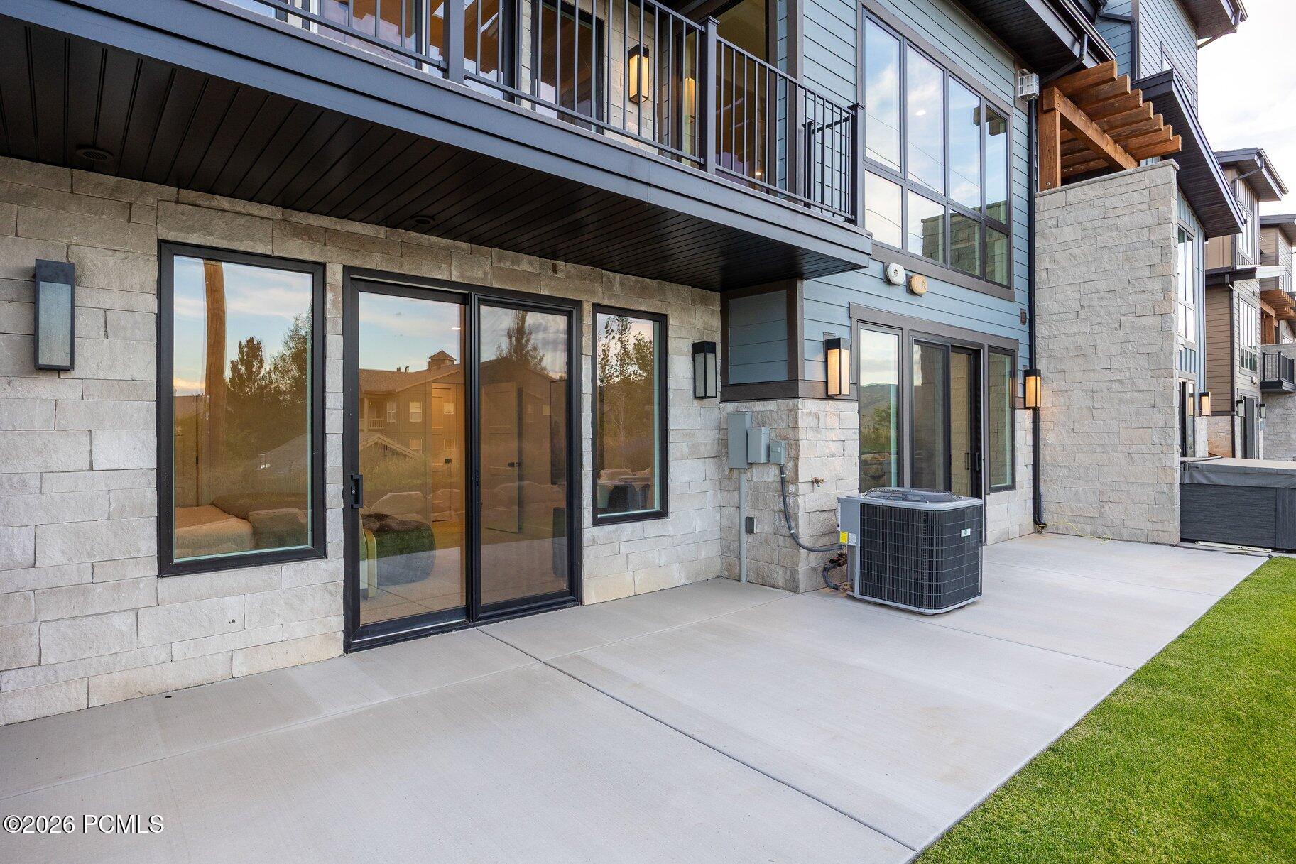 Modern home exterior with stone walls, large windows, balconies, and a wooden staircase.