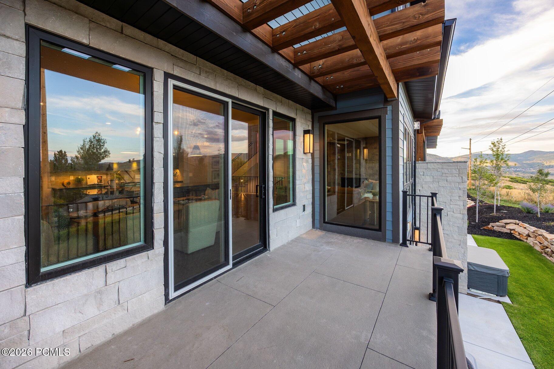 Modern home terrace with exposed timber beams, large windows, and views of distant hills.