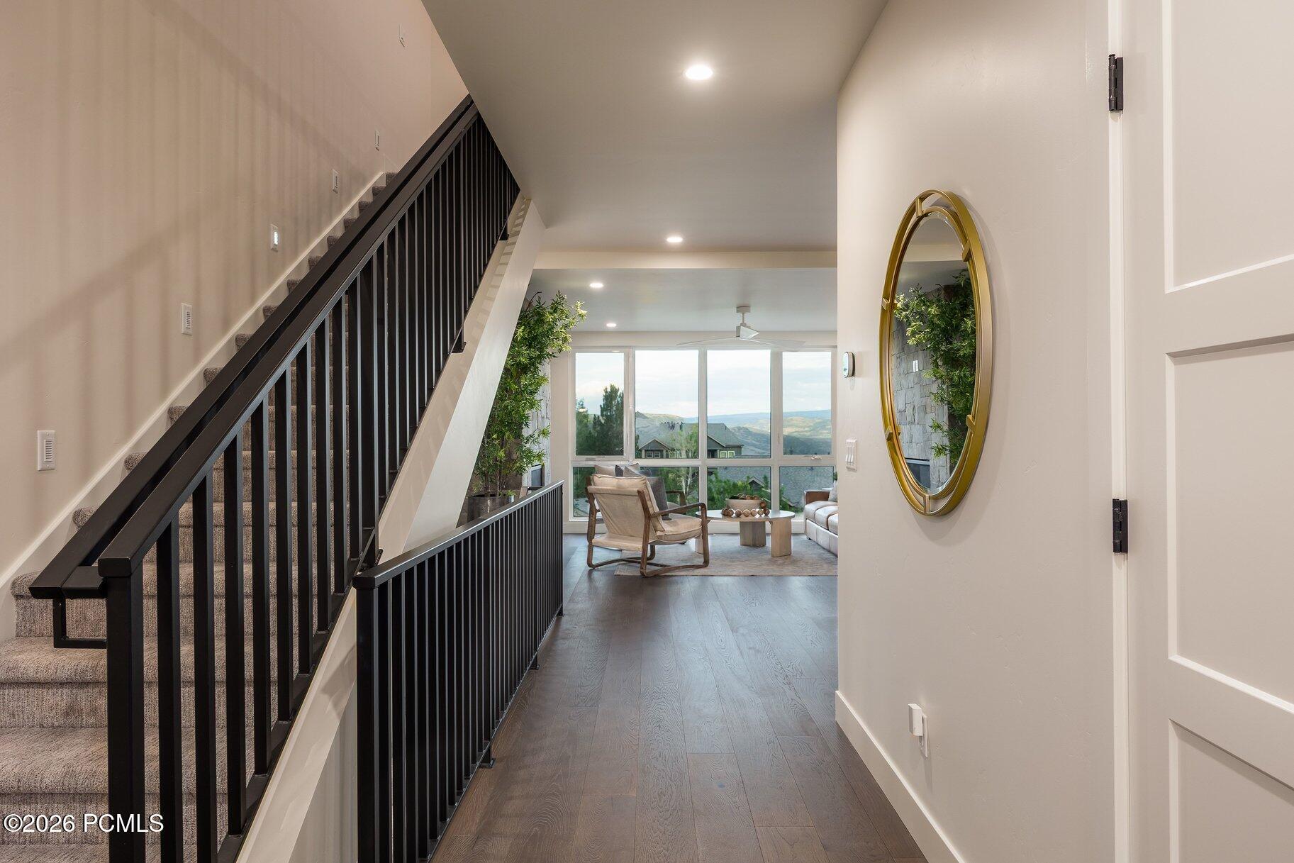 Entry hall with black-railed staircase opening to a sitting area with wide hillside-view windows.