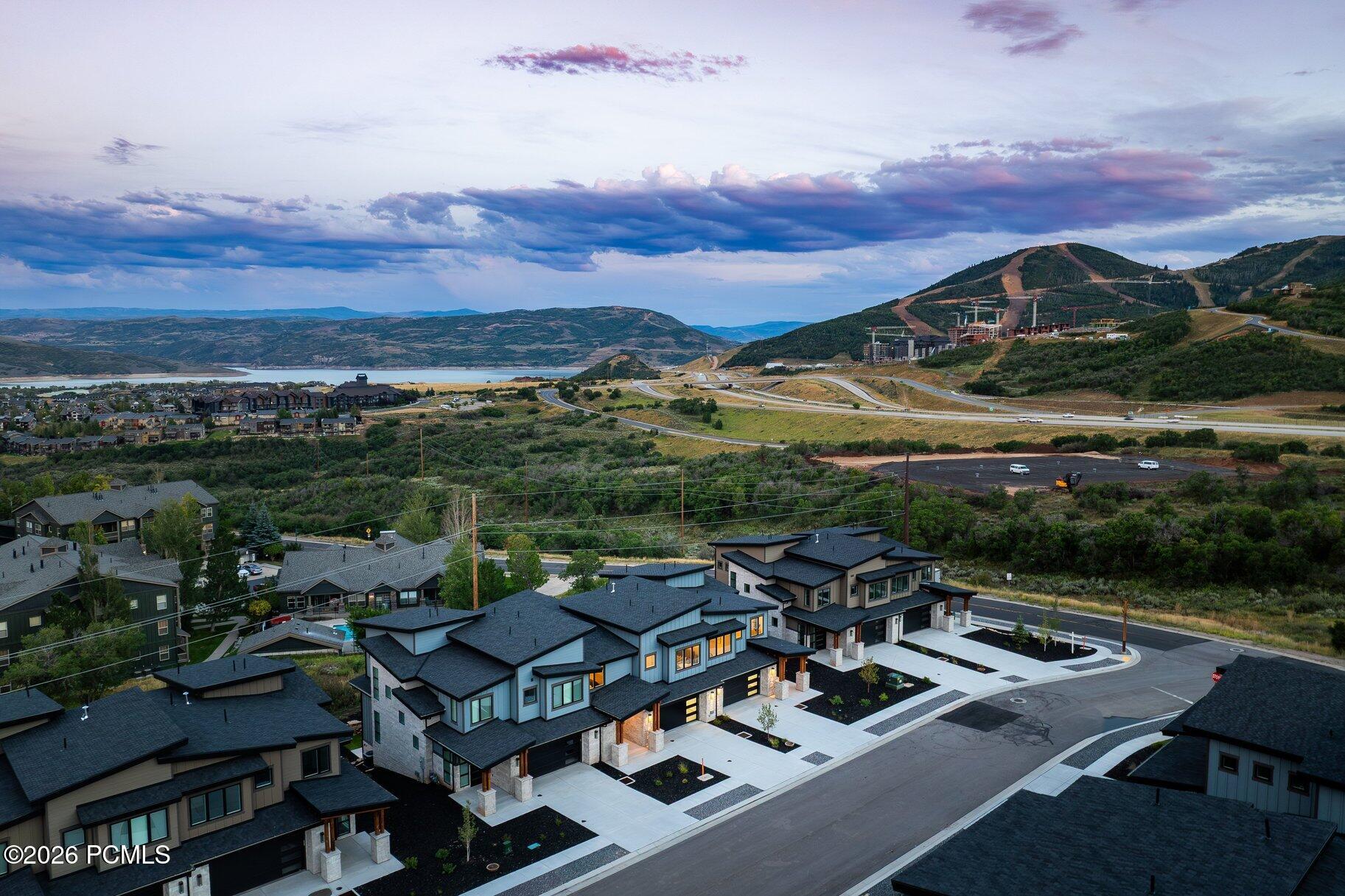 Aerial view of modern homes overlooking a lake and mountain resort beneath colorful clouds.