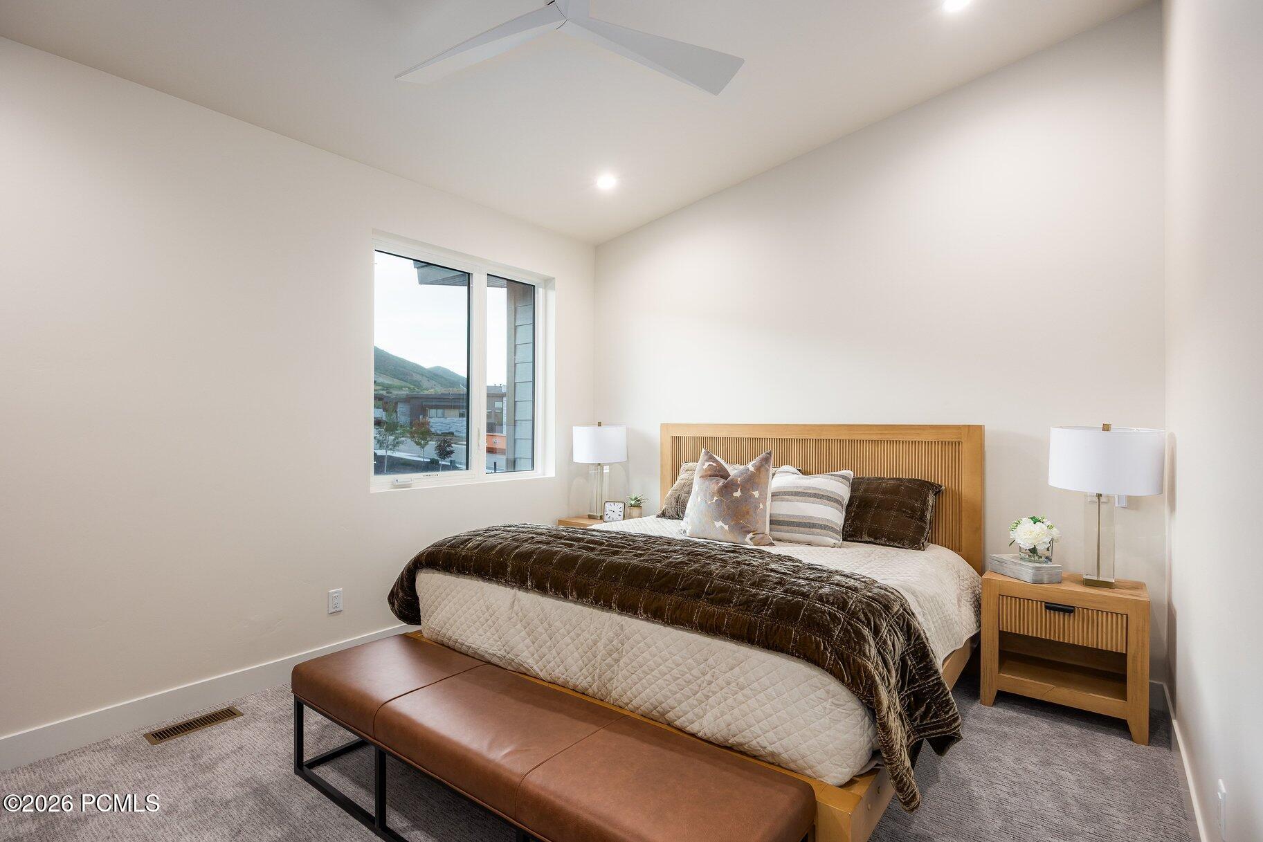 Furnished bedroom with a king bed, slatted wood headboard, leather bench, and mountain views through the window.