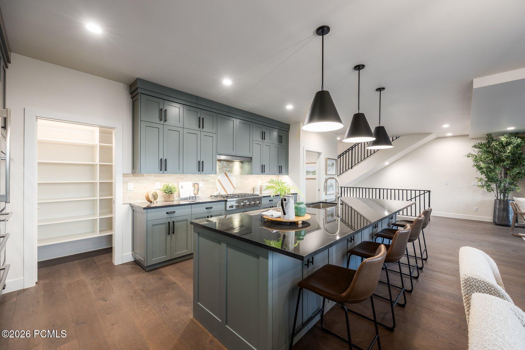 Modern kitchen with blue-gray cabinets, a large island, dark counters, and three pendant lights.
