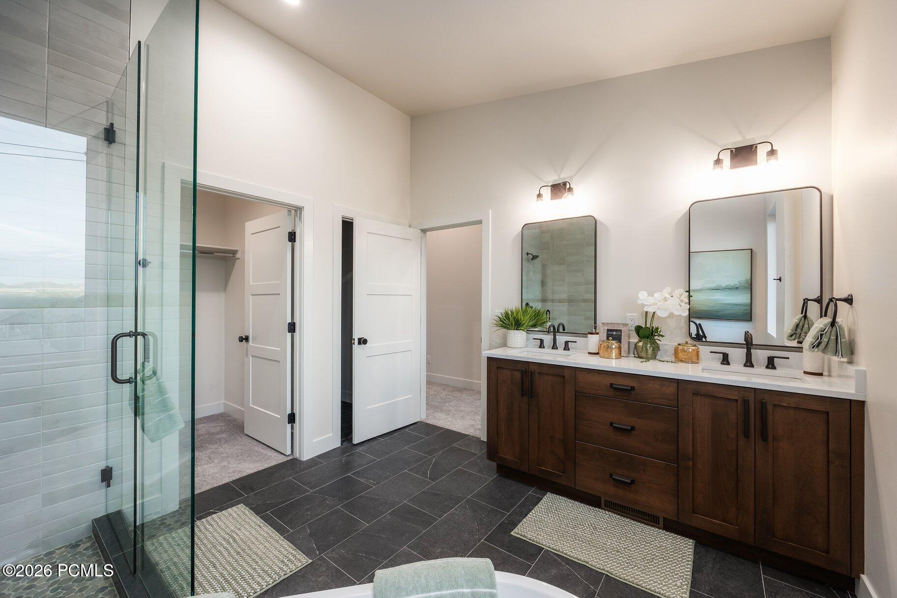 Bathroom with a dark wood double vanity, glass shower, and dark tile flooring.