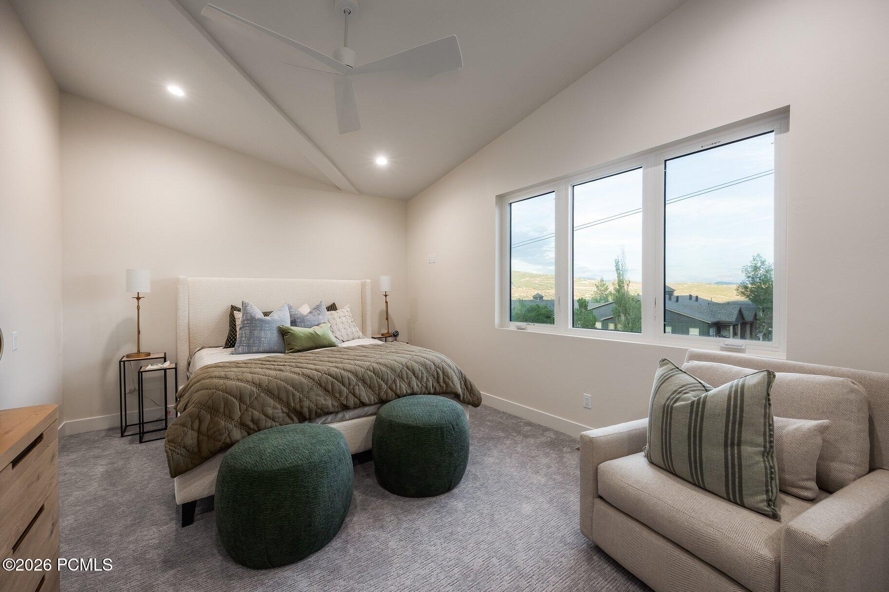 Furnished bedroom with a vaulted ceiling, wide windows, and views of distant water.