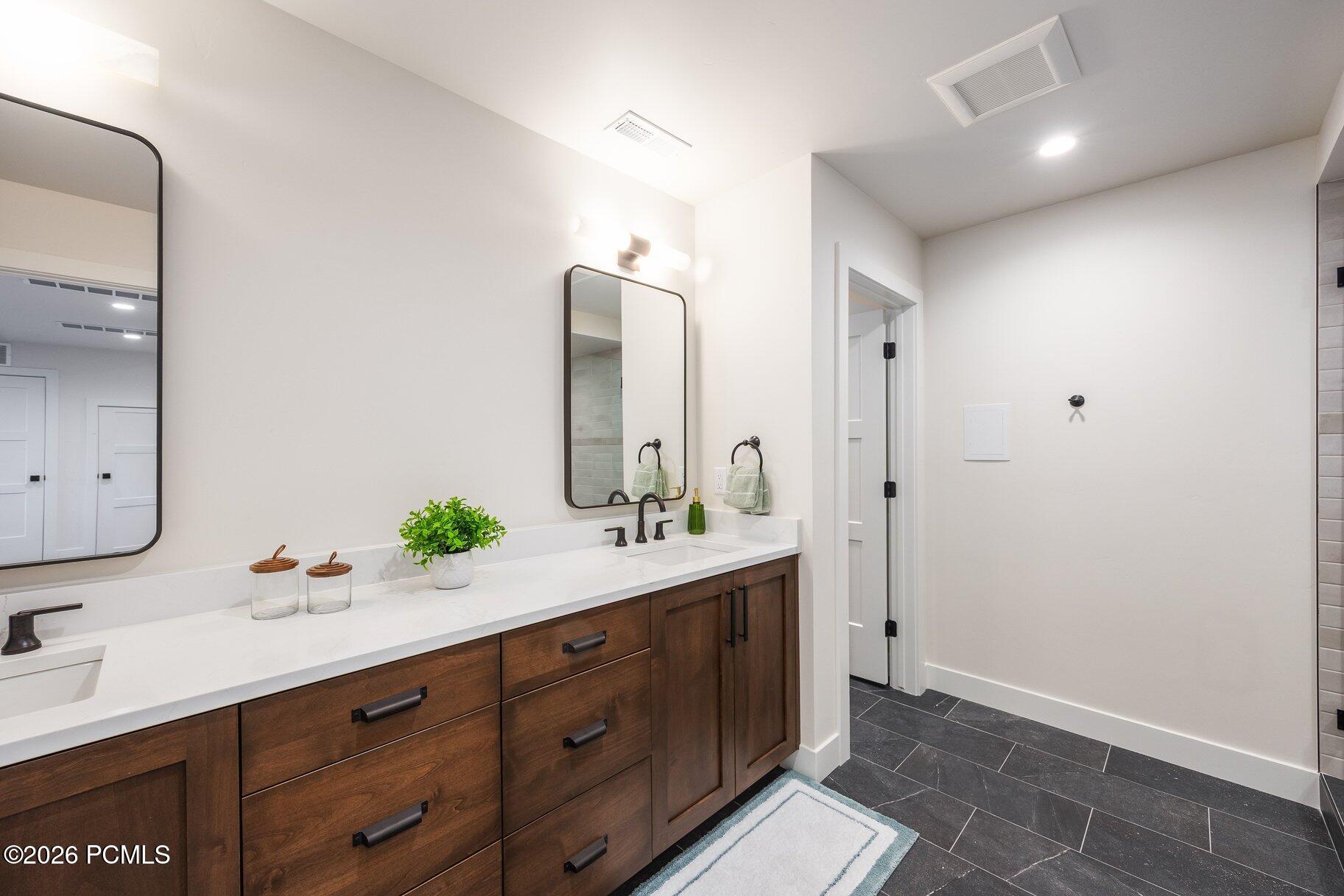 Bathroom vanity with dark wood cabinets, white counters, two sinks, and black-framed mirrors.