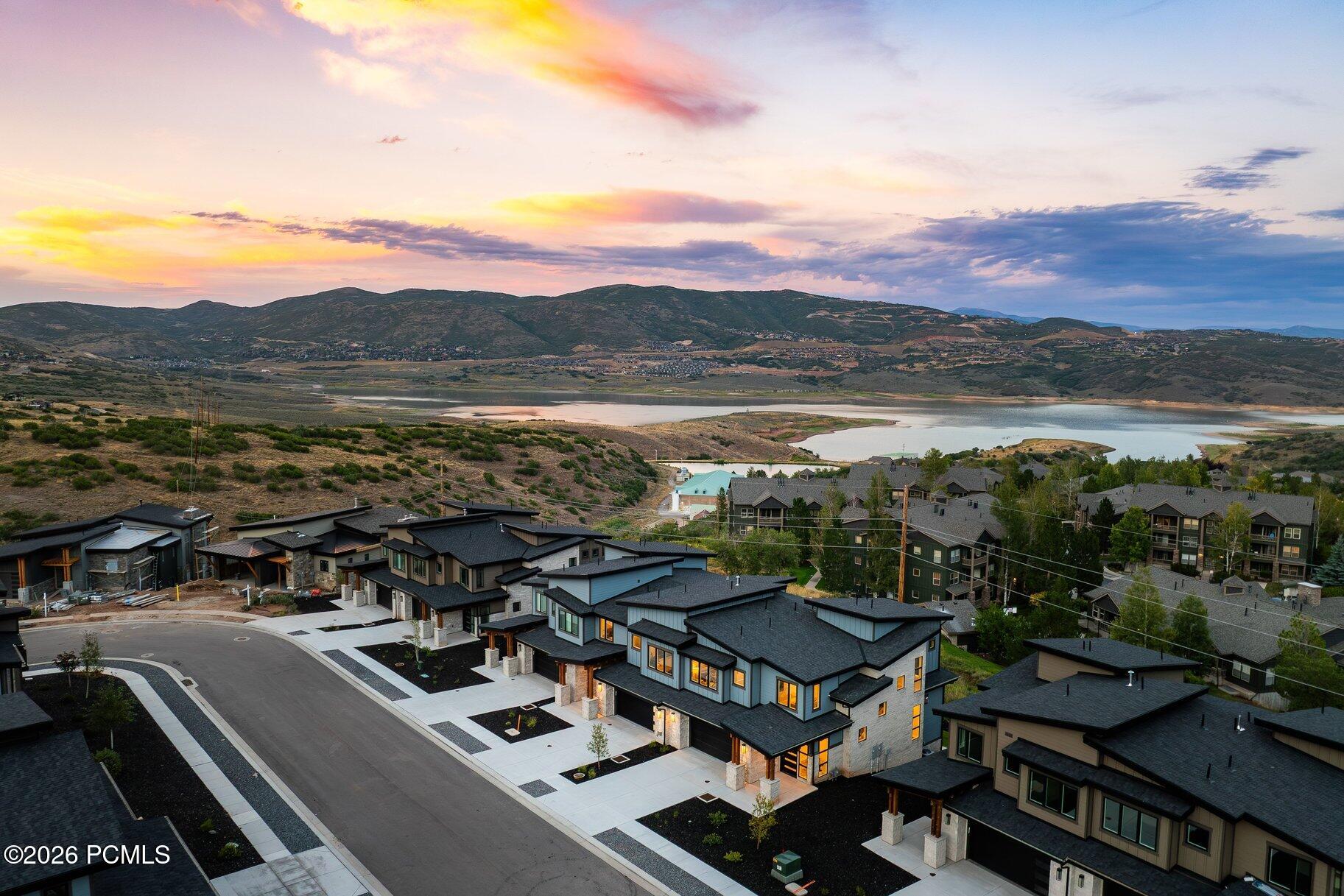 Modern homes overlook a reservoir and mountain valley beneath a colorful sunset sky.