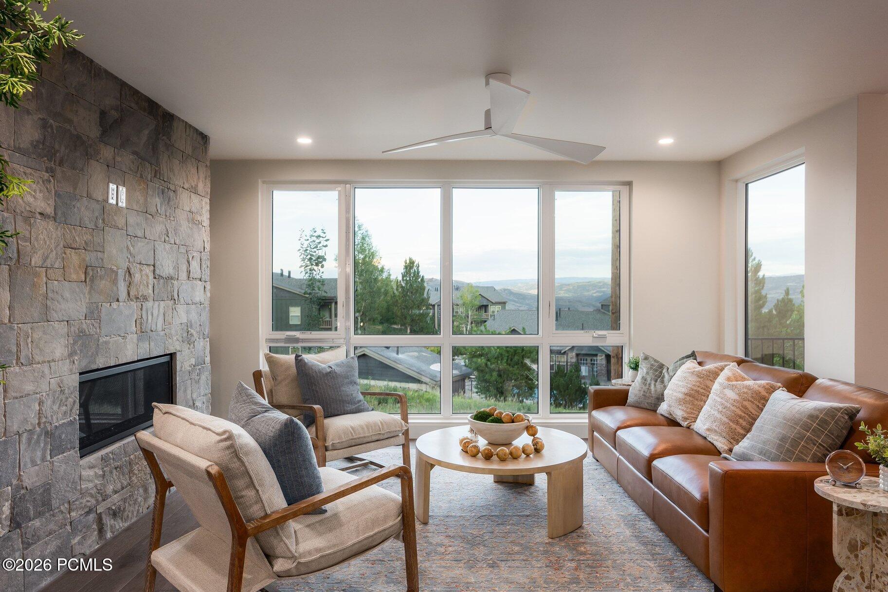 Living room with a stone fireplace, leather sectional, and expansive windows overlooking distant hills.