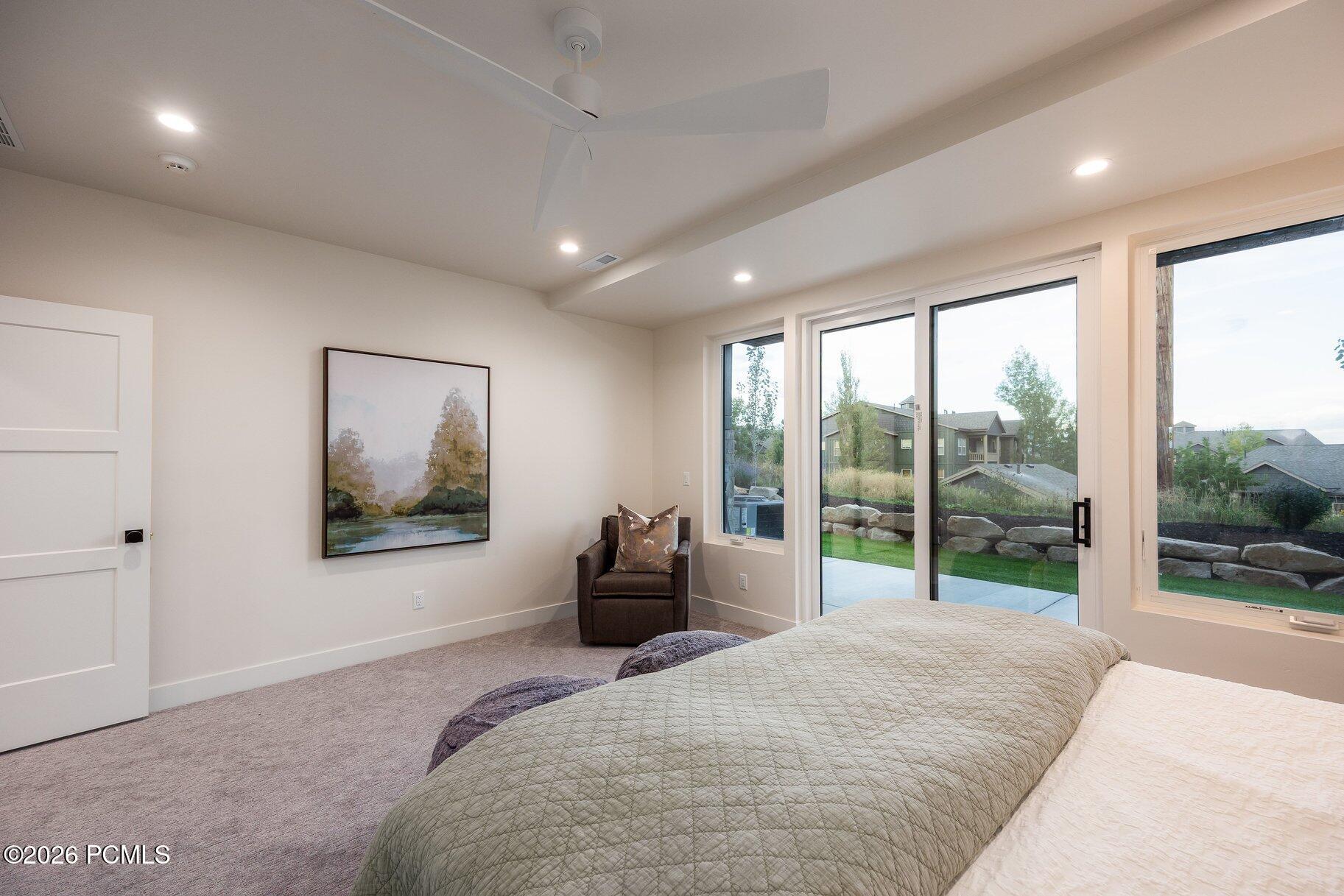 Bedroom with a large bed and sliding glass doors overlooking a patio and landscaped yard.