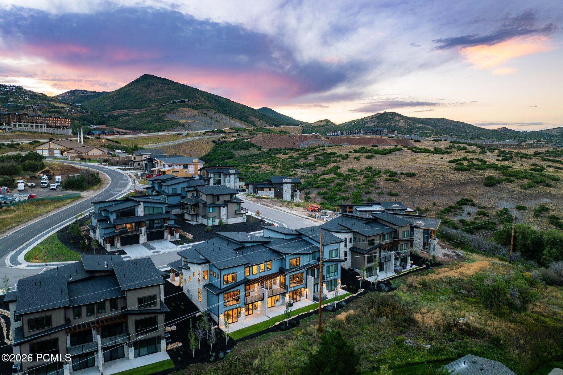 Aerial view of modern homes in mountain foothills beneath a colorful sunset sky.