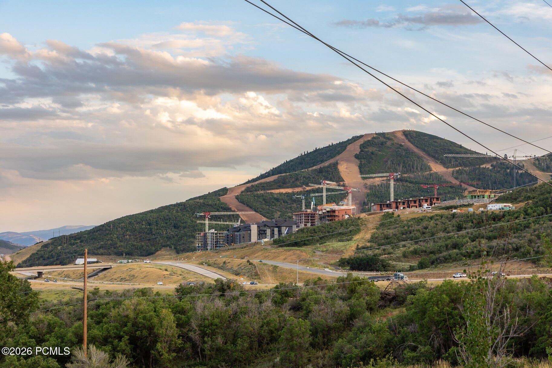 Wooded mountain with ski runs and hillside construction beneath a cloudy sky.