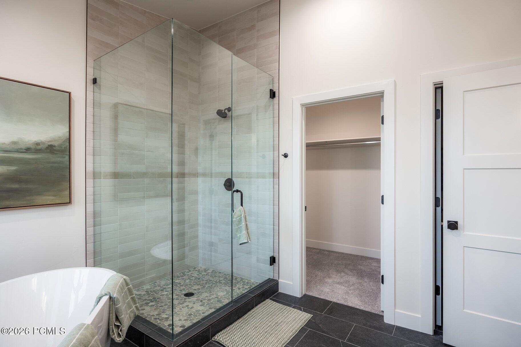 Staged bathroom with a glass walk-in shower, pebble-mosaic floor, and partially visible soaking tub.