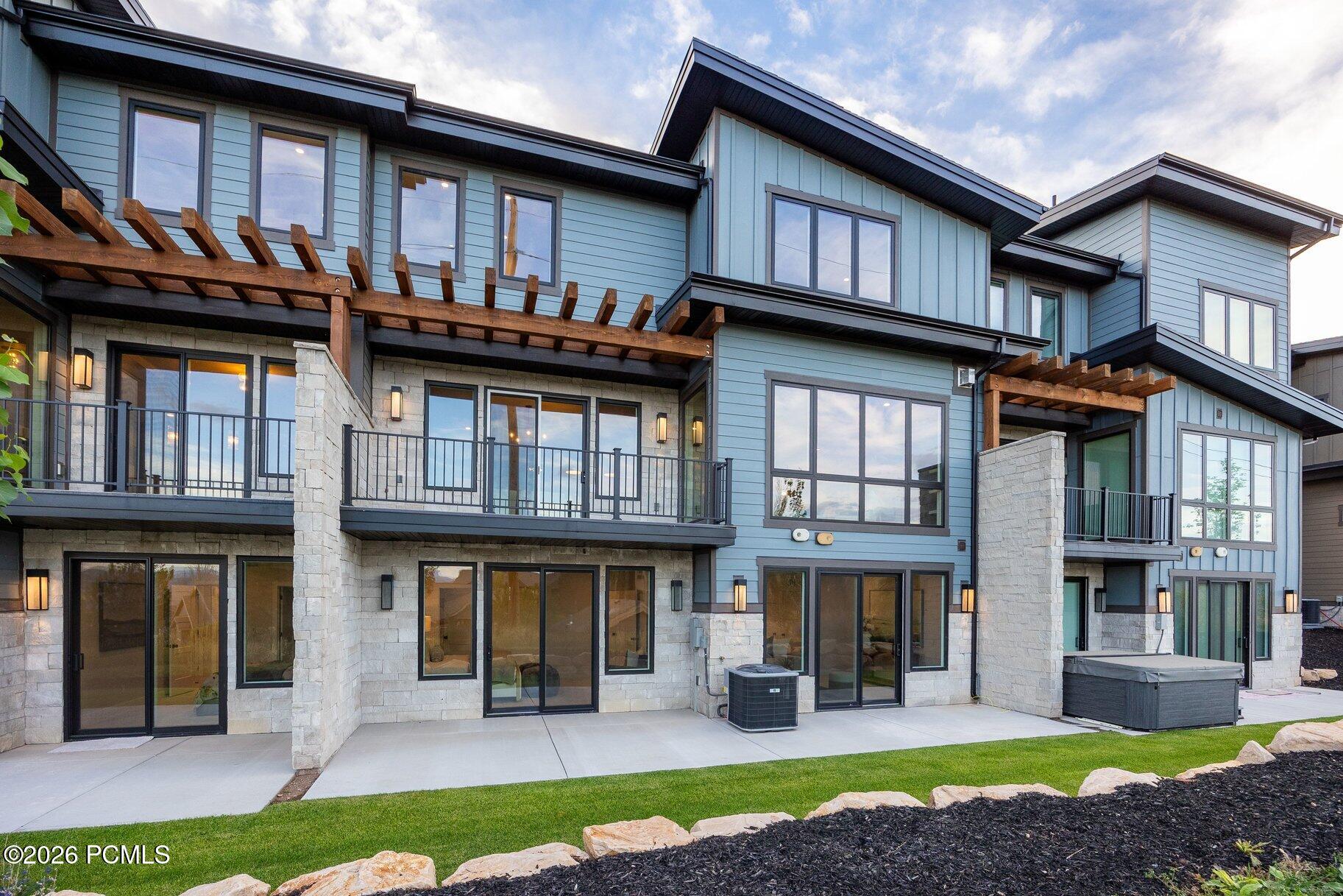 Modern blue-gray home exterior with stonework, balconies, timber pergolas, and a covered hot tub.