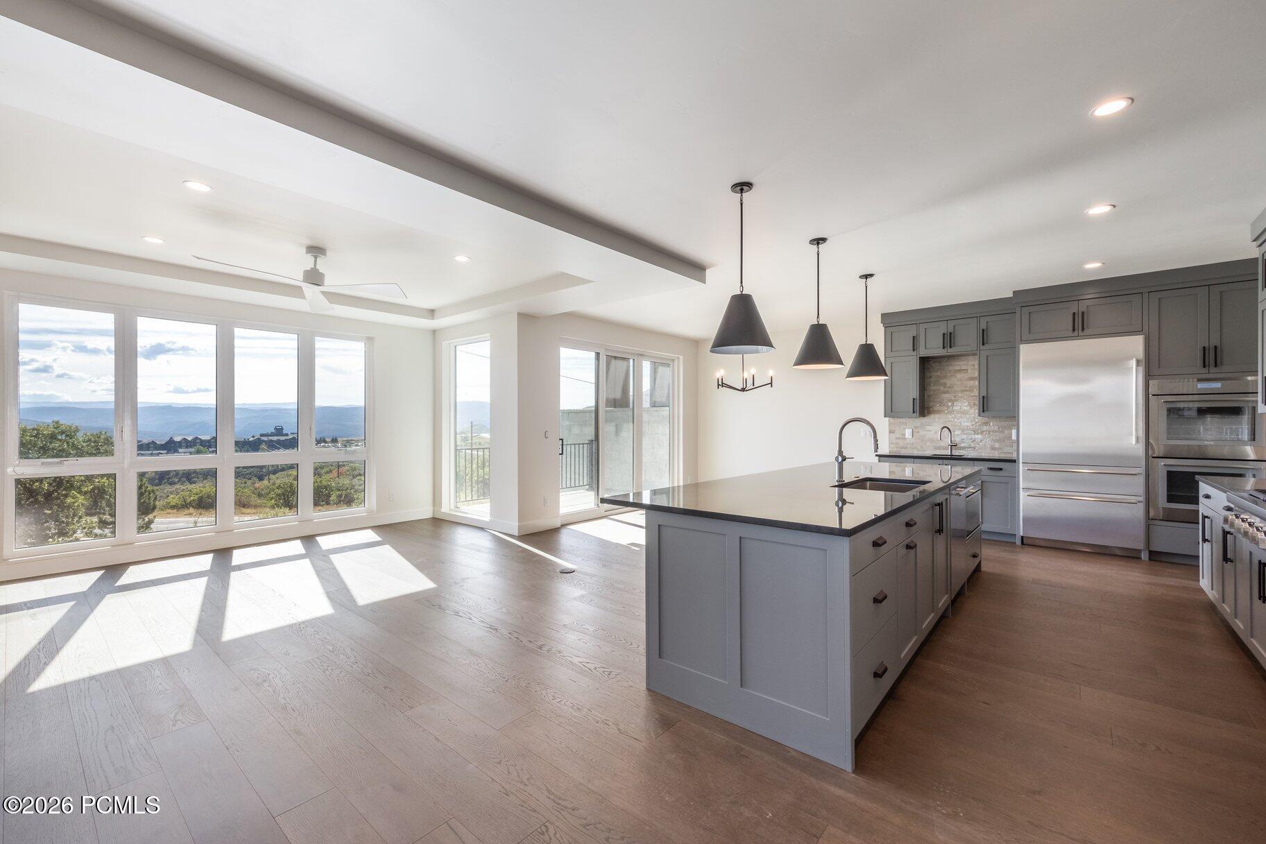 Open kitchen with gray cabinets and island, large windows overlooking wooded hills and distant mountains.
