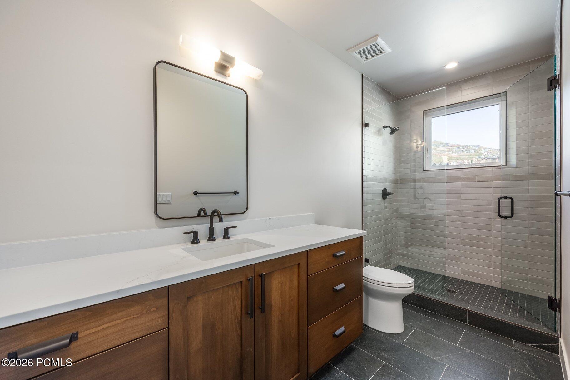 Modern bathroom with a wood vanity, black fixtures, and a glass shower beside a hillside-view window.