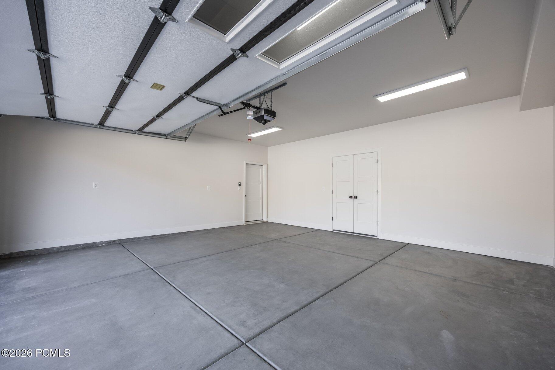 Empty garage with a concrete floor, overhead door, and white double doors.