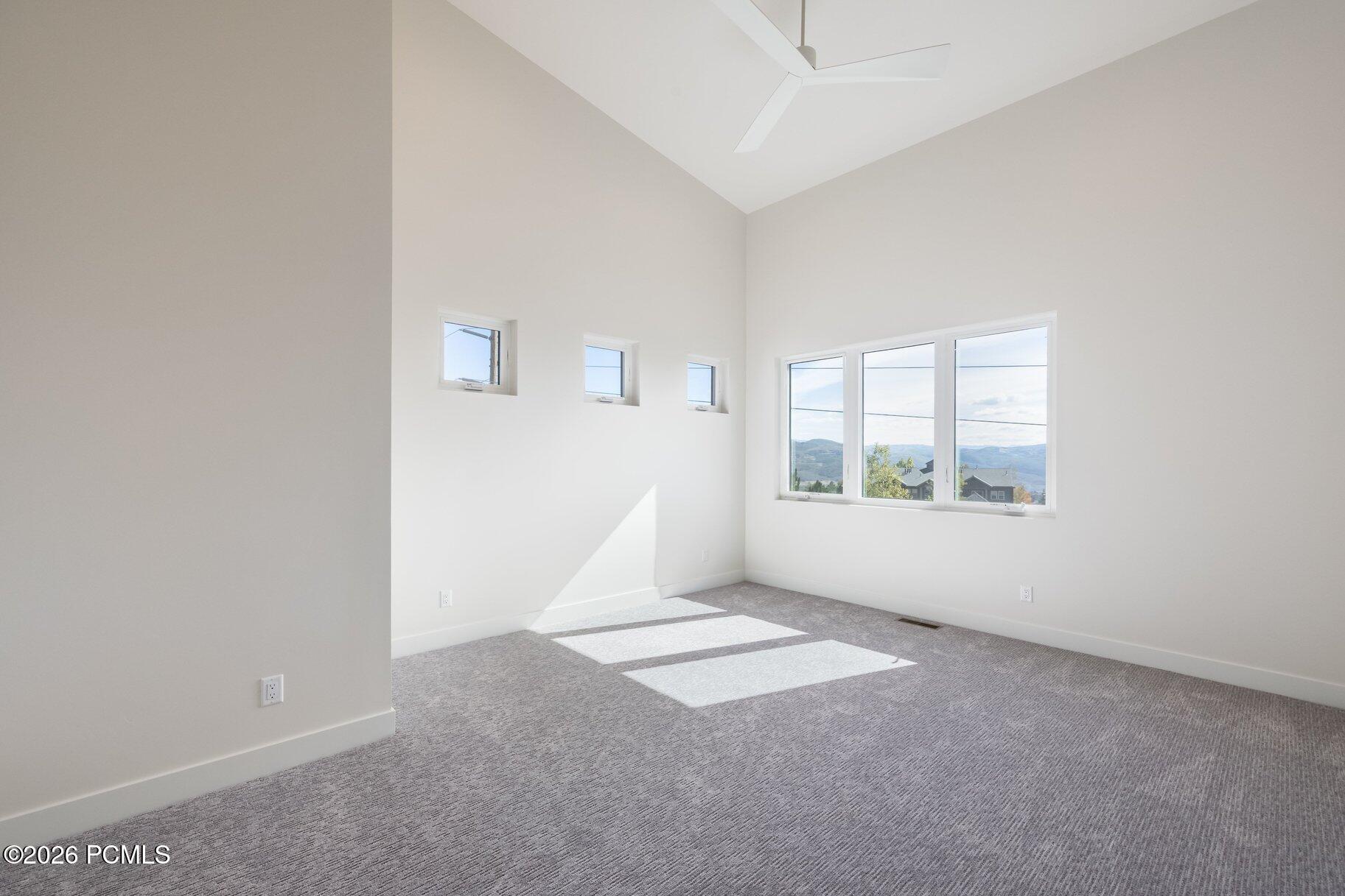 Empty carpeted bedroom with a vaulted ceiling and mountain views through the windows.