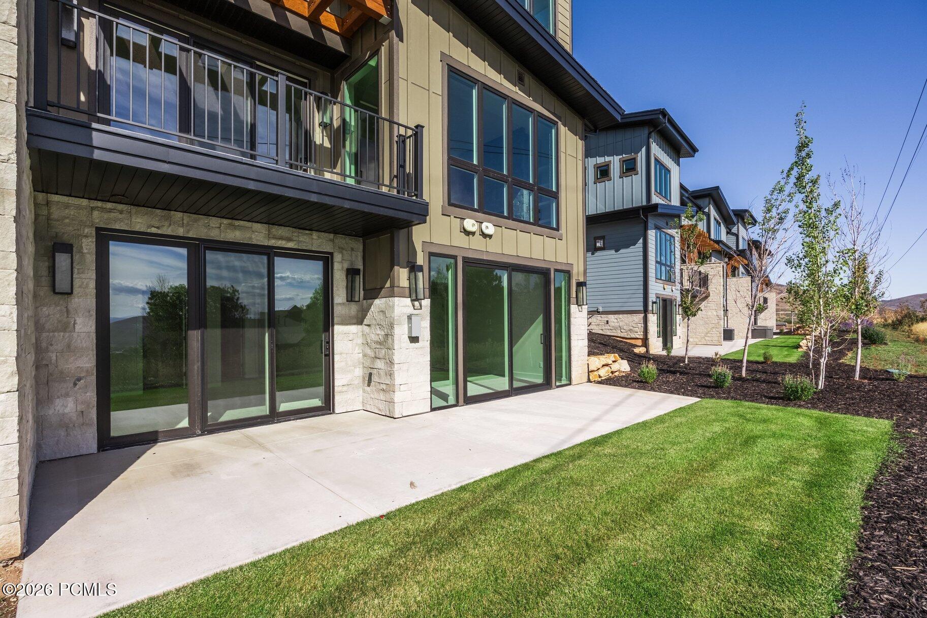 Modern home exterior with stone accents, large windows, and a concrete patio beside a green lawn.