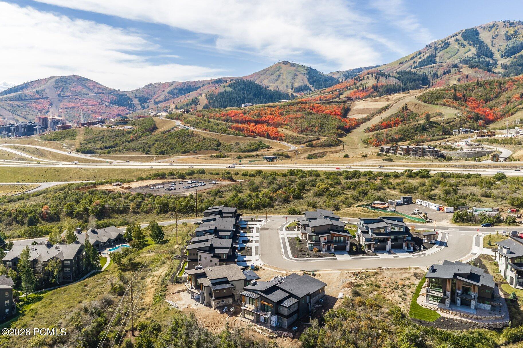 Aerial view of modern homes below mountain slopes covered in autumn foliage.