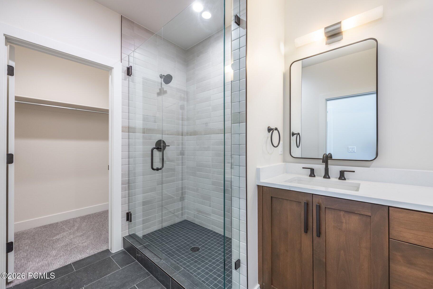 Modern bathroom with a glass walk-in shower, dark wood vanity, and open closet doorway.
