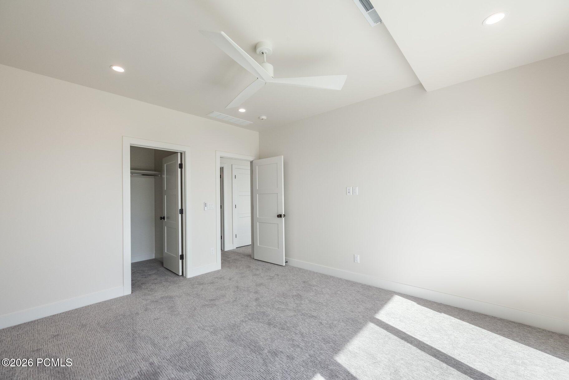 Vacant bedroom with gray carpet, a ceiling fan, and sunlight across the floor.