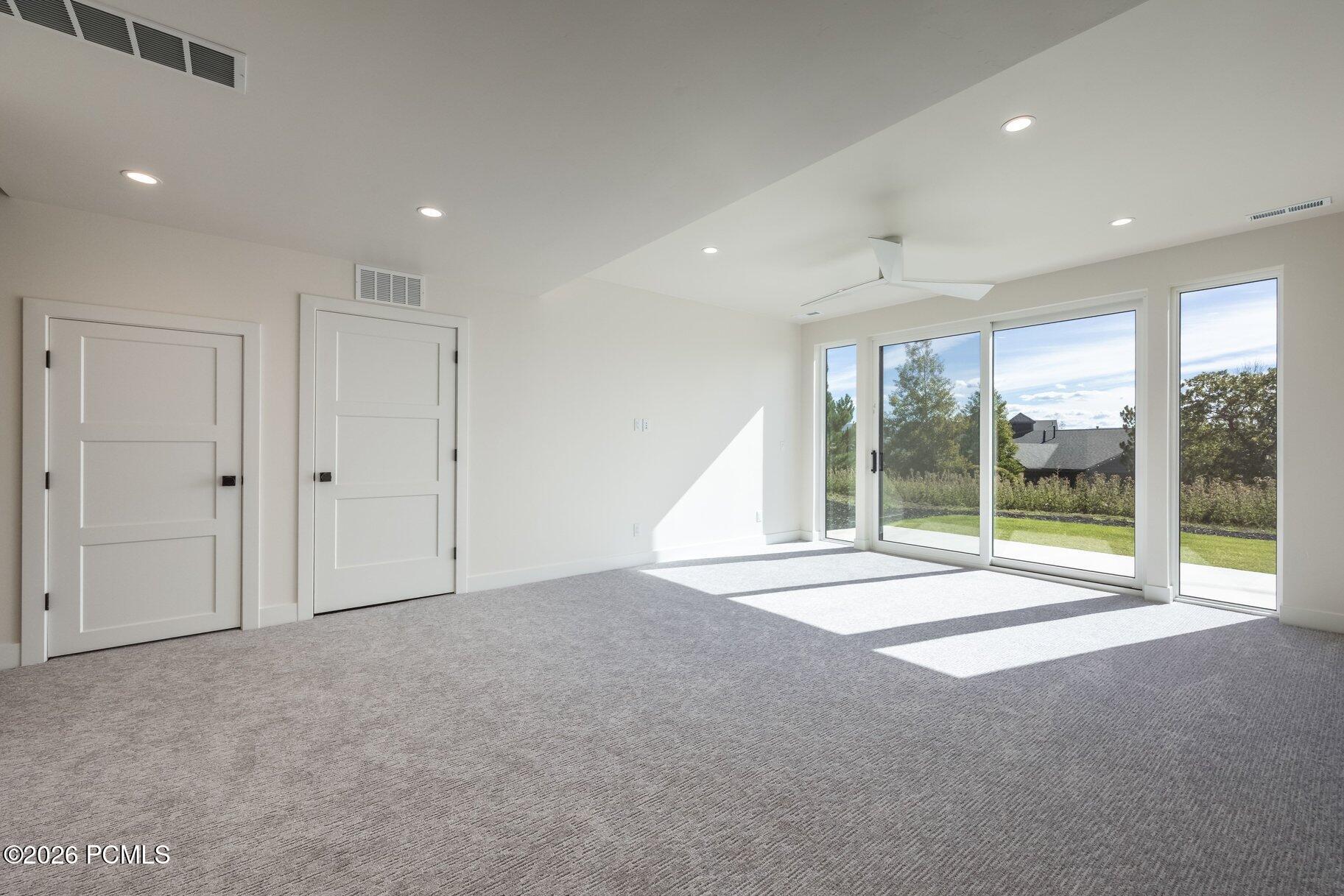 Vacant carpeted room with large sliding glass doors opening to a patio and lawn.