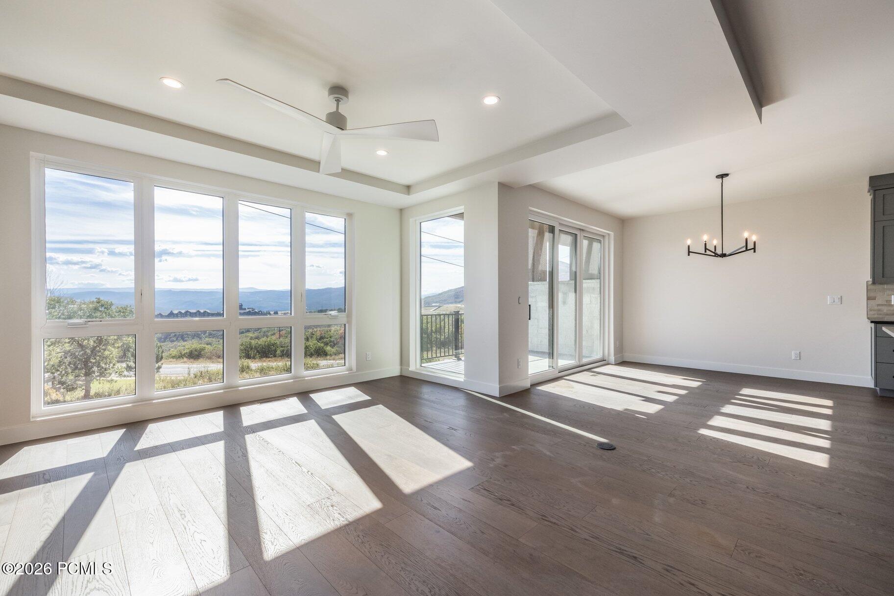 Vacant living and dining area with expansive windows, mountain views, and sunlight across pale wood floors.
