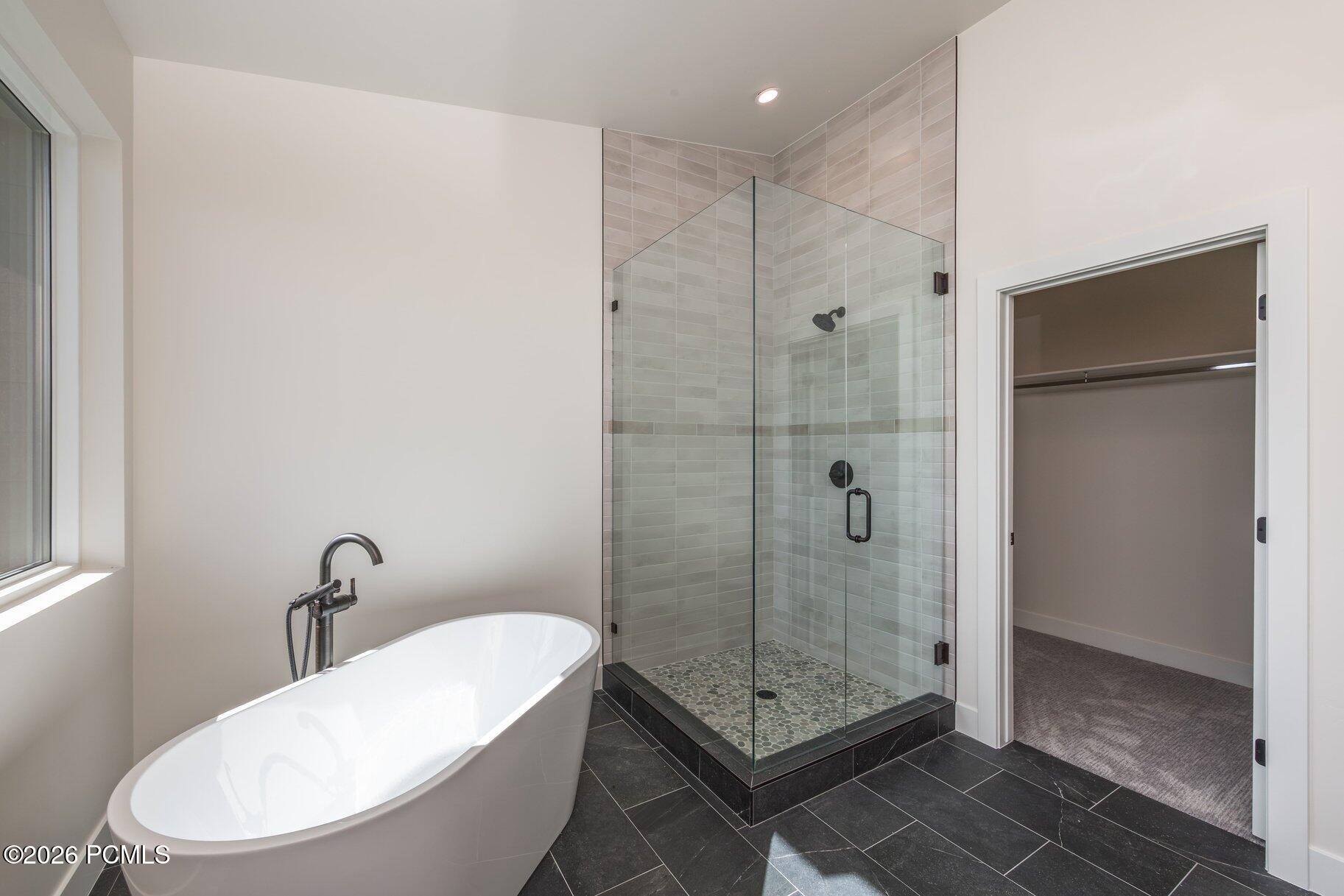 Modern bathroom with a freestanding tub, glass shower, pebble floor, and doorway to a walk-in closet.