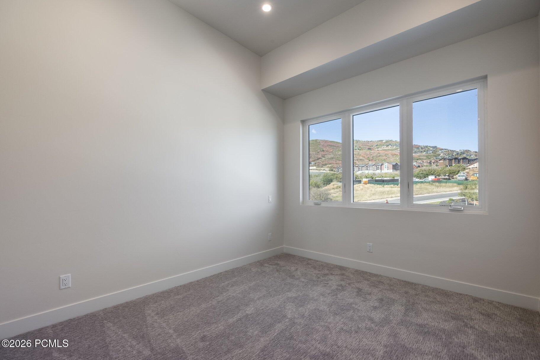 Empty carpeted bedroom with a wide window overlooking hillside homes.