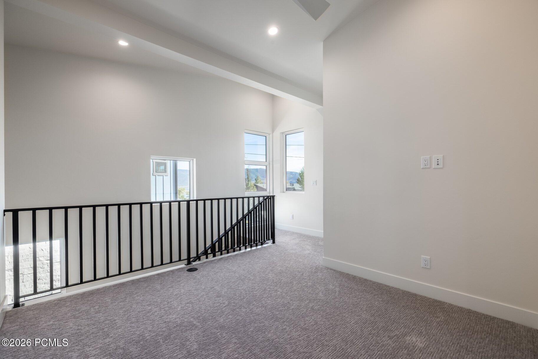 Unfurnished carpeted loft landing with black railing and mountain views through tall windows.